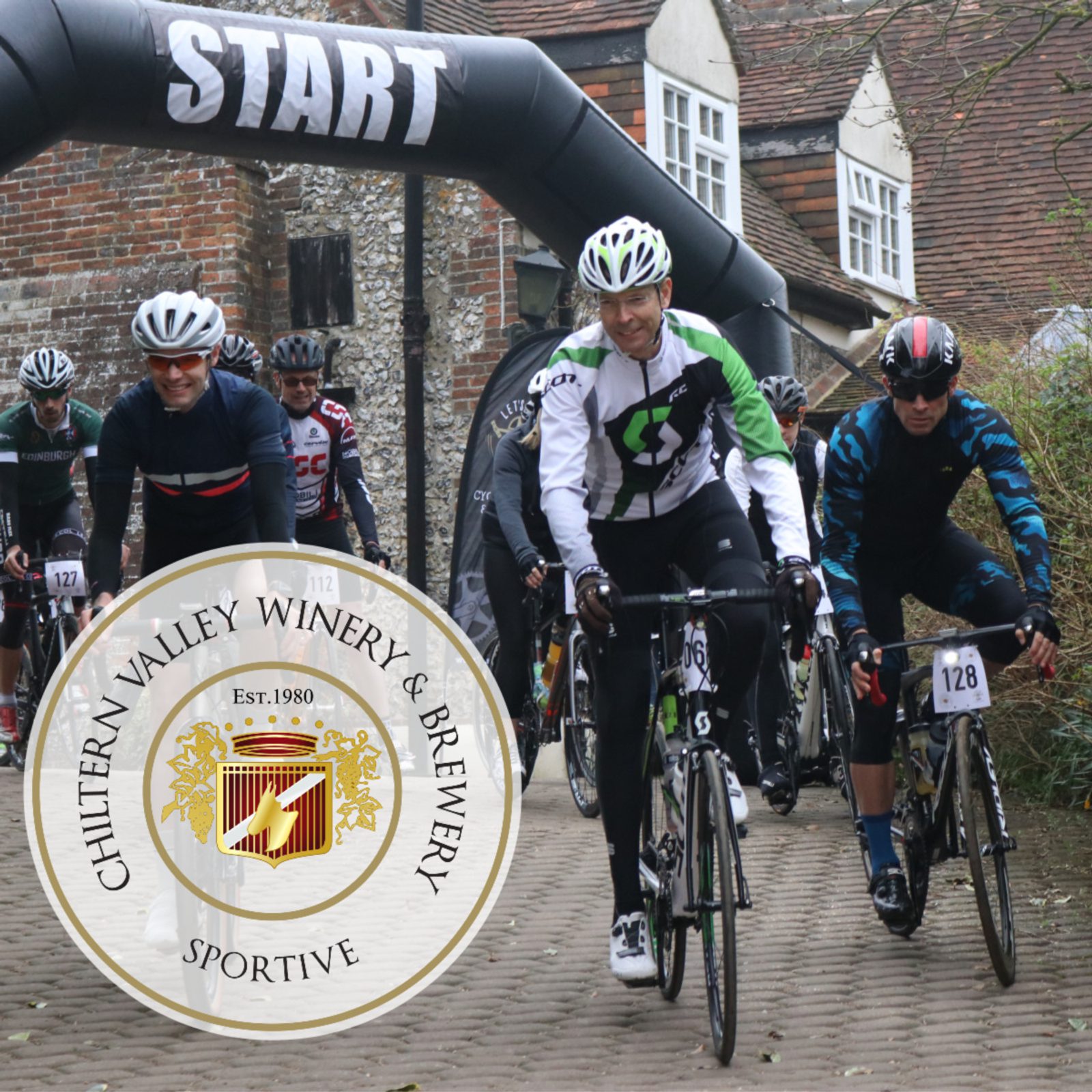 Cyclists in gear riding through a start line under an archway at an outdoor event. There is a large circular logo for Chiltern Valley Winery & Brewery Sportive in the foreground. The background features a rustic building with brick walls and greenery.