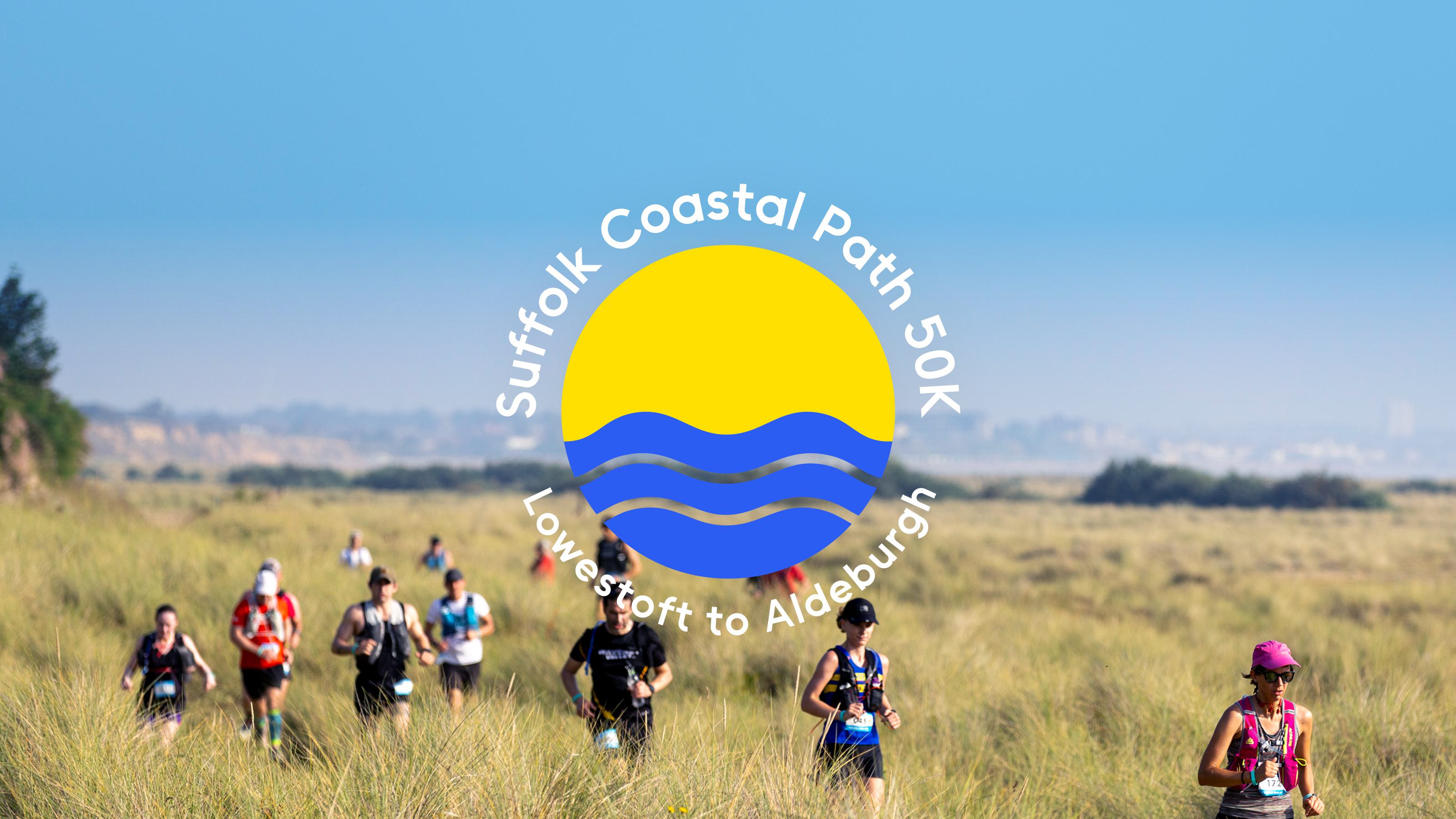 A group of runners participate in the Suffolk Coastal Path 50k race from Lowestoft to Aldeburgh. They are running through a grassy field under a clear blue sky. The event's logo, featuring a yellow sun and blue waves, is overlaid on the image.