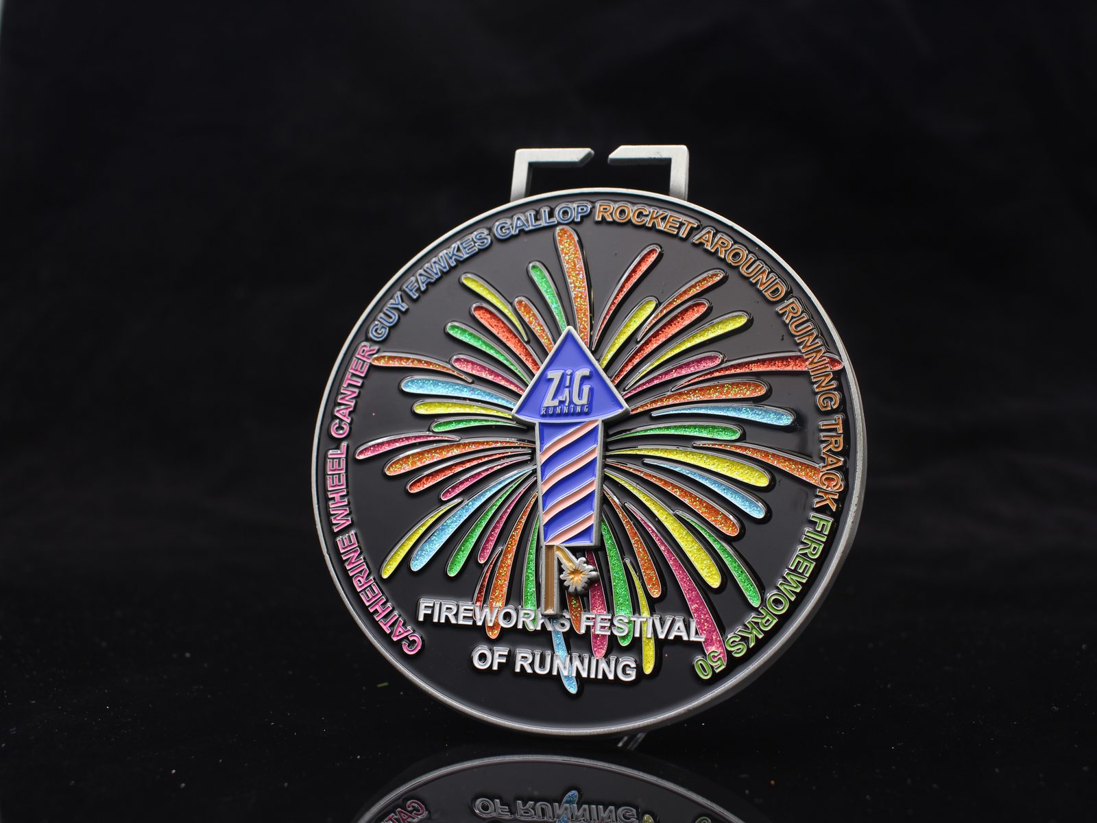 A round medal with a colorful firework and rocket design, labeled “Z&K Events.” Text around the edge reads “Catherine Wheel, Canter, Guy Fawkes Gallop, Rocket Around Running Track, Fireworks Festival of Running.”.