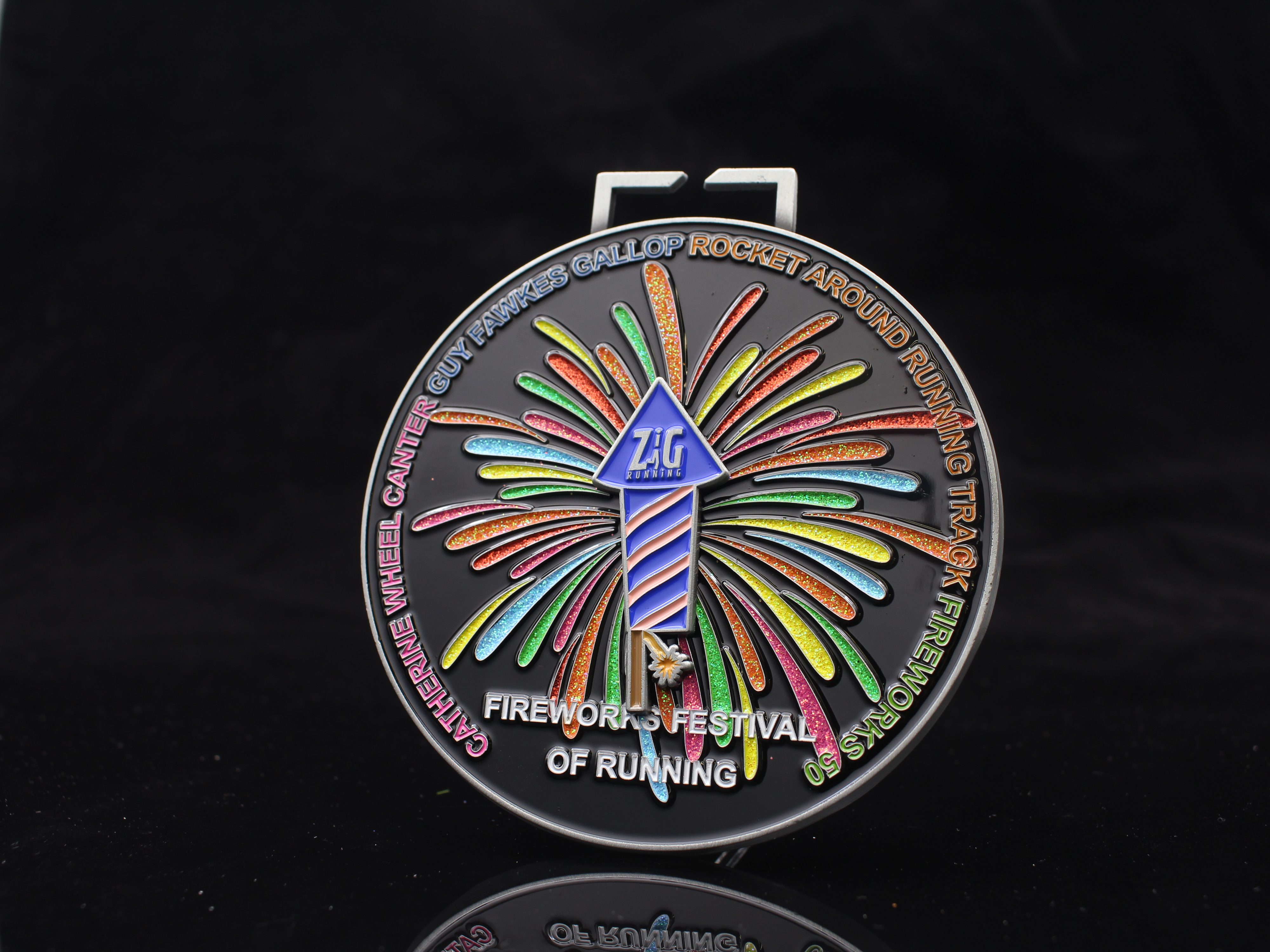 A colorful medal with a rocket and fireworks design, labeled "Z&L RACES" and "FIREWORKS FESTIVAL OF RUNNING." The edge lists: "Catherine Wheel, Canter, Guy Fawkes Gallop, Rocket Around Running Track, Fireworks 5K.