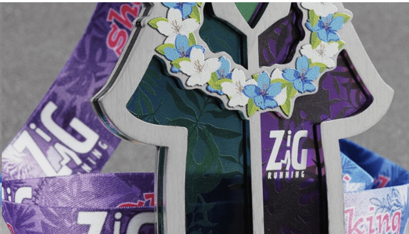 A close-up image of a metallic trophy shaped like a person adorned with a lei made of blue and white flowers. The trophy has the text "Zig Running" on it, and a colorful, patterned ribbon in shades of purple and blue is attached to it.