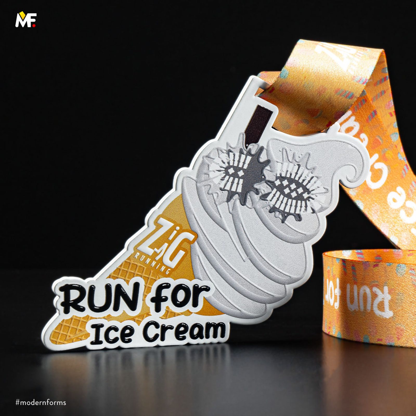 A medal shaped like an ice cream cone with a gold waffle cone and gray swirled ice cream, overlaid with the text "RUN for Ice Cream." The medal hangs from an orange ribbon with a white pattern. Logo "MF" at the top left corner. #modernforms in the corner.