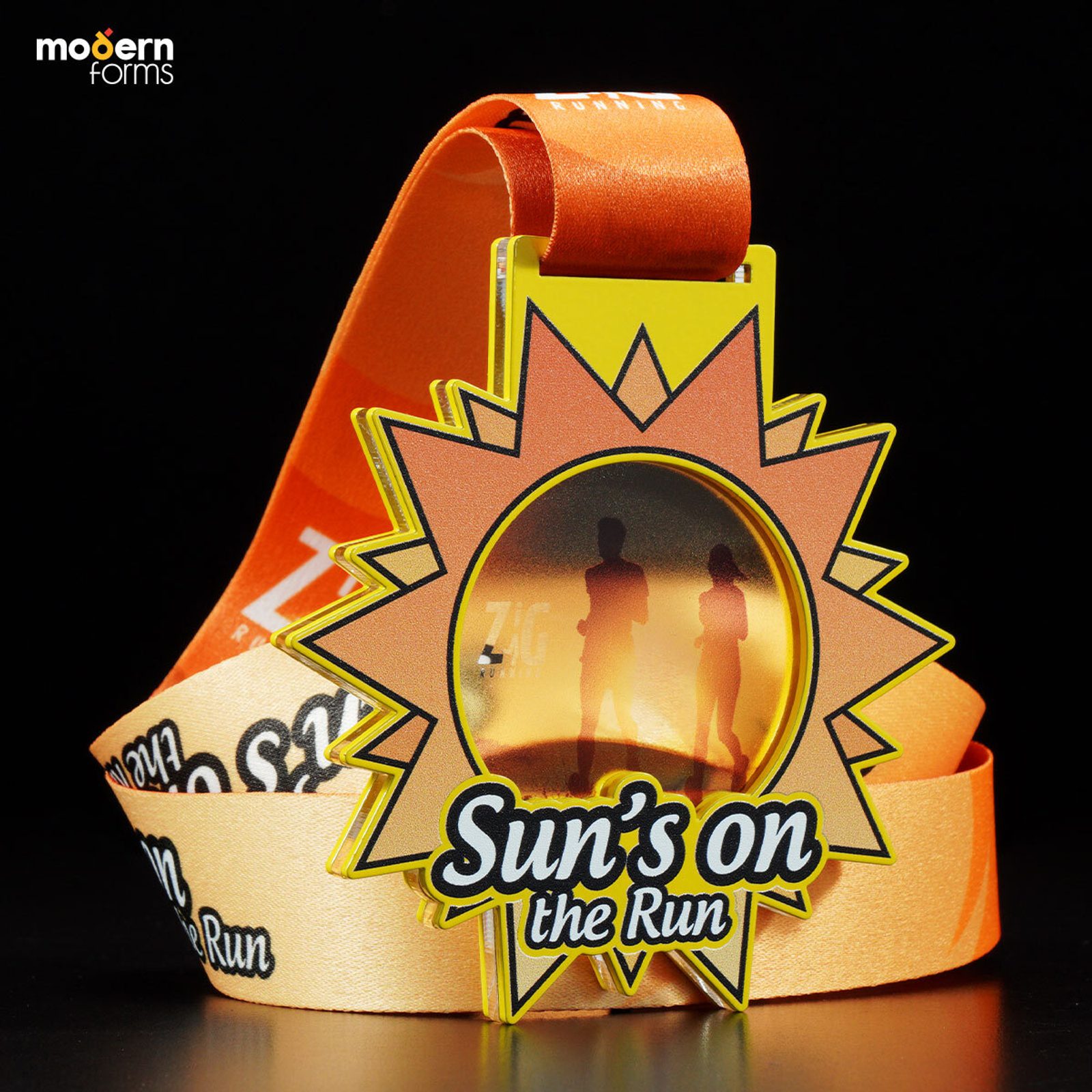 A bright yellow and orange medal with a sun shape and a silhouette of two runners in the center. The text reads "Sun’s on the Run" and it's attached to a matching orange ribbon with the same text. The background is black, highlighting the medal's vibrant colors.
