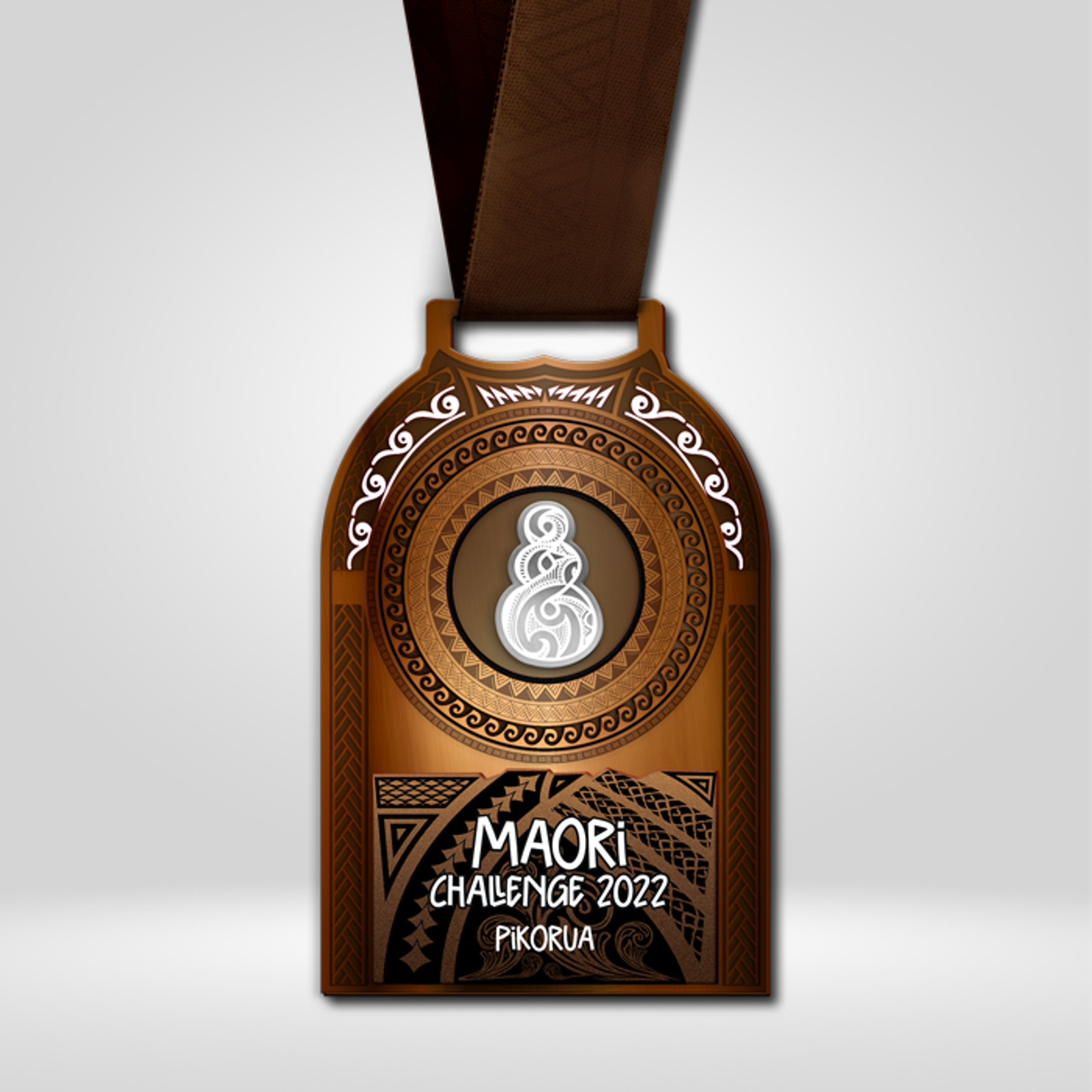 A medal with a brown ribbon features intricate MΔori designs and symbols. In the center is a circular motif with traditional patterns. Text reads "MΔori Challenge 2022 PΔ«rorua" at the base in white against a dark background with additional MΔori artwork.
