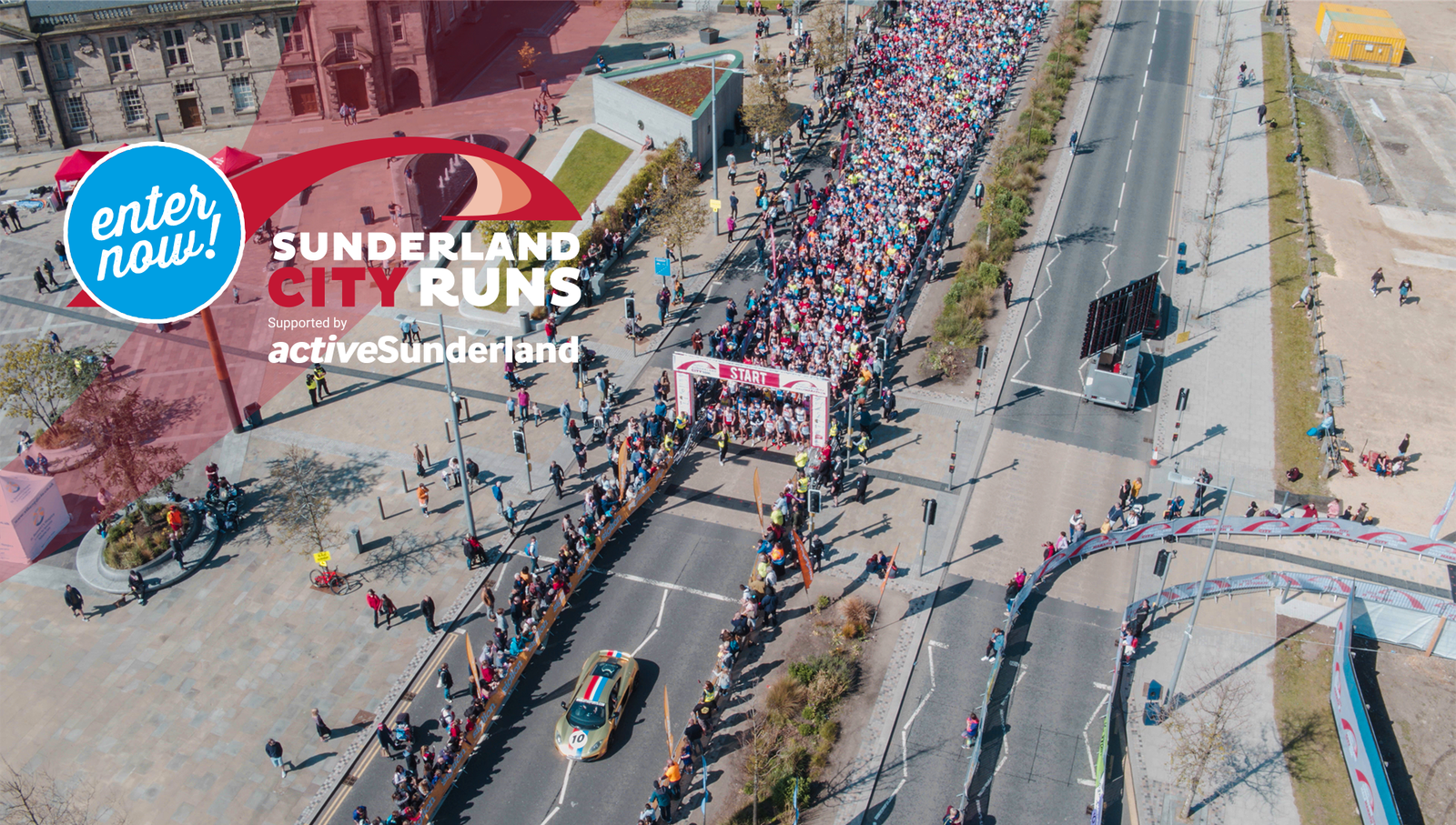 Aerial view of the Sunderland City Runs event with a large crowd of participants running on a wide street. A colorful banner hangs over the road at the starting line. There are spectators on the sides and an "Enter Now" sign in the top-left corner.