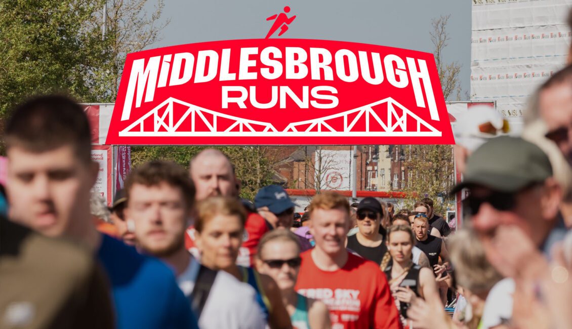 A crowd of runners outdoors with a large red and white "Middlesbrough Runs" logo featuring a bridge graphic displayed prominently above them.