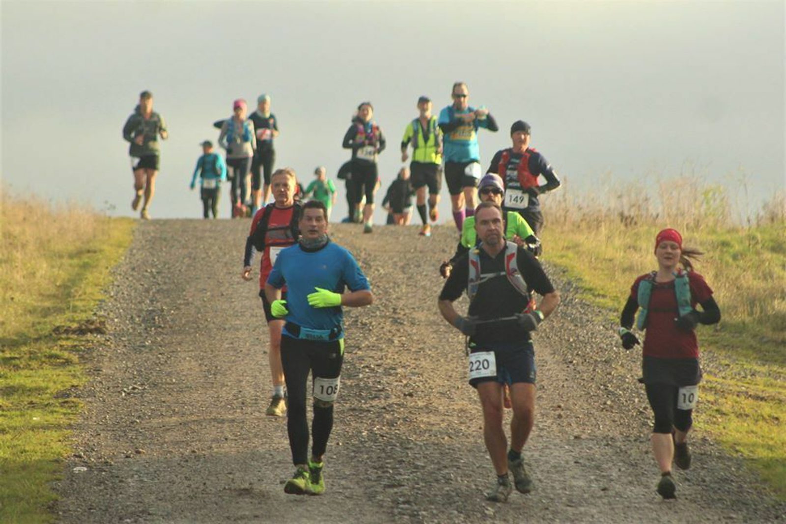 A group of runners participating in a race on a gravel path. The runners are dressed in various colorful athletic gear and are moving both up and down a slight incline. They appear focused and determined as they make their way along the route.