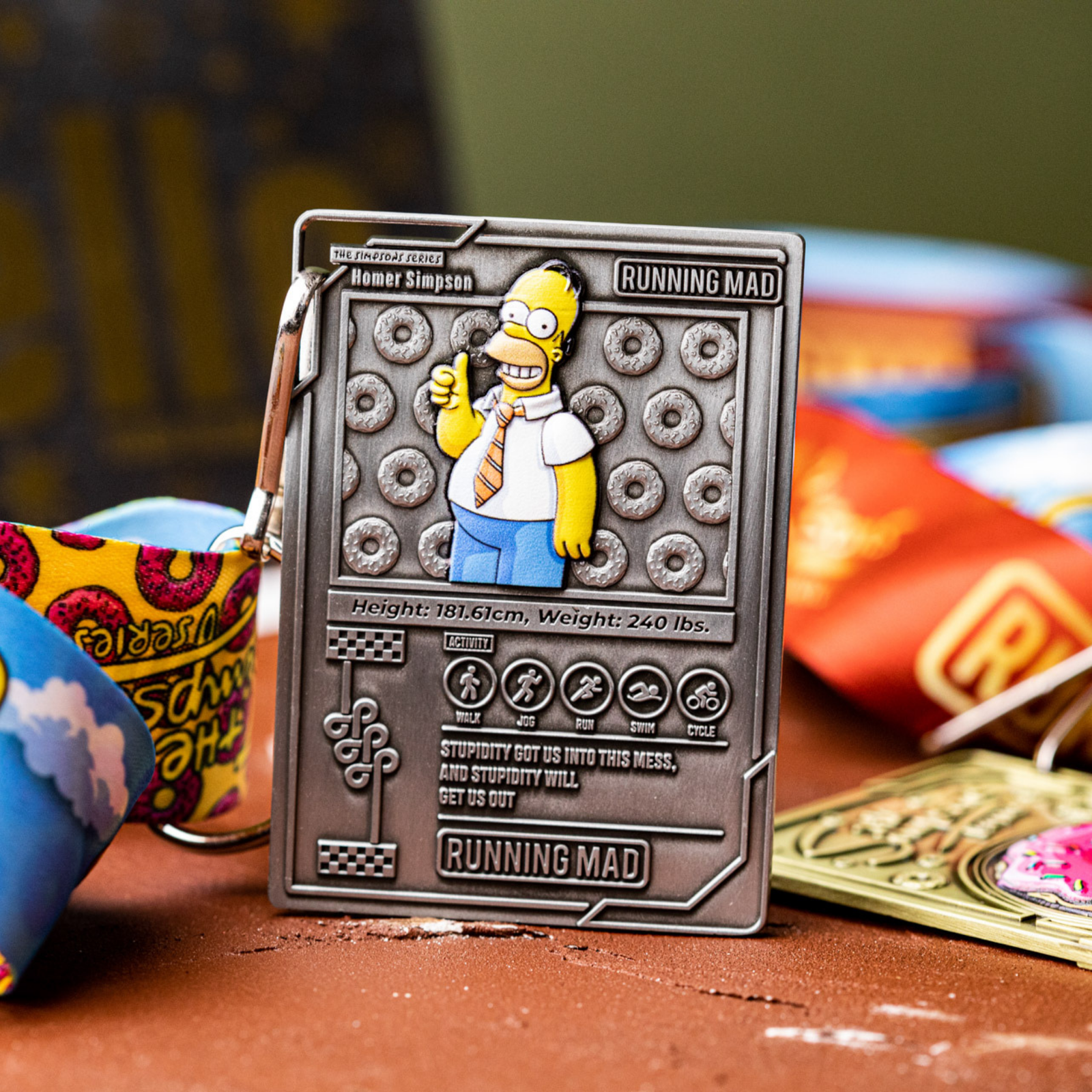A metal card featuring a cartoon character with text details. The card is labeled "Homer Simpson" with stats like height and weight. Brightly colored lanyard attached. Surrounding elements include vibrant designs and text.