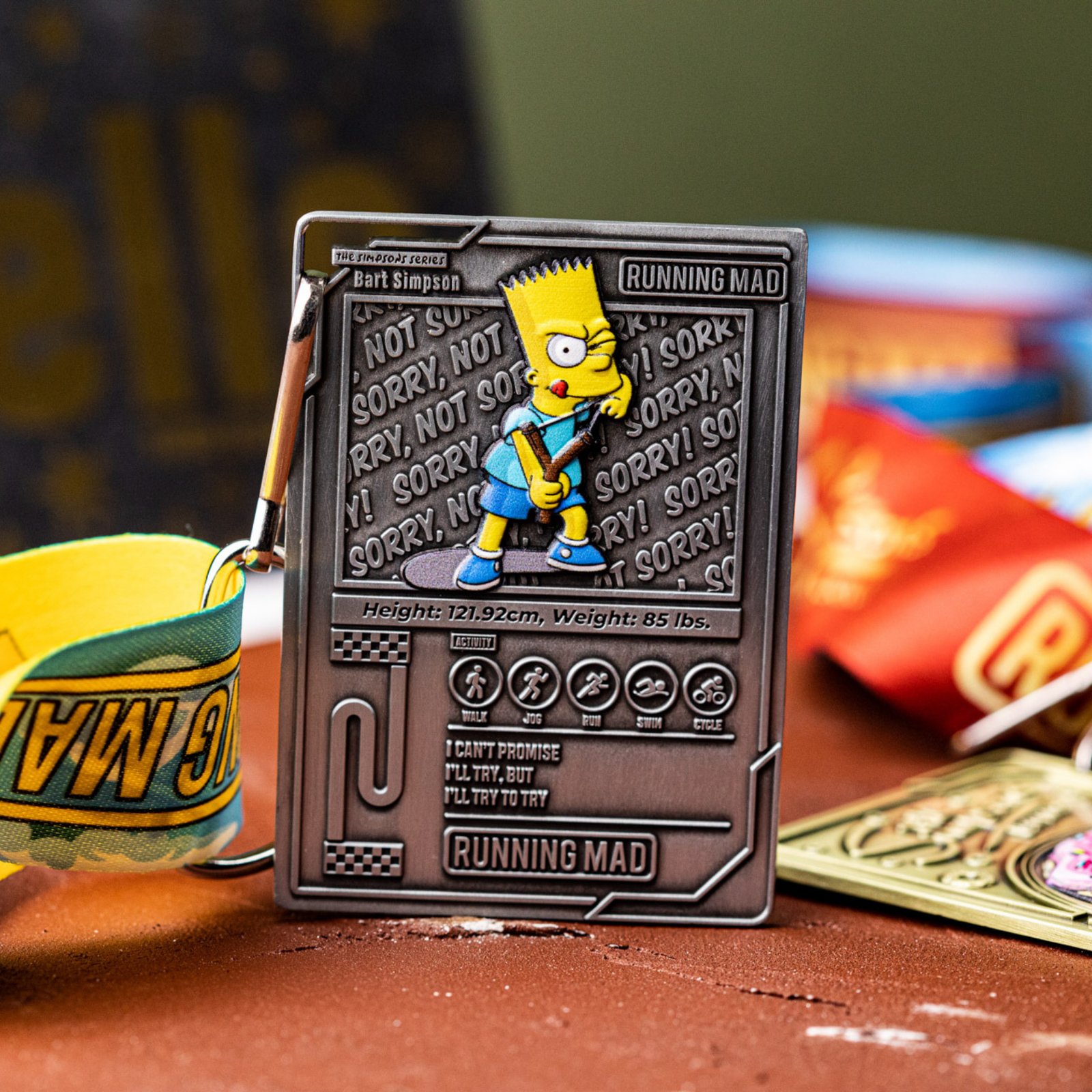 A metal keychain featuring a cartoon character with spiky hair holding a slingshot. The background includes the text "SORRY! NOT SORRY!" repeatedly. Bright colors and playful design elements are visible.