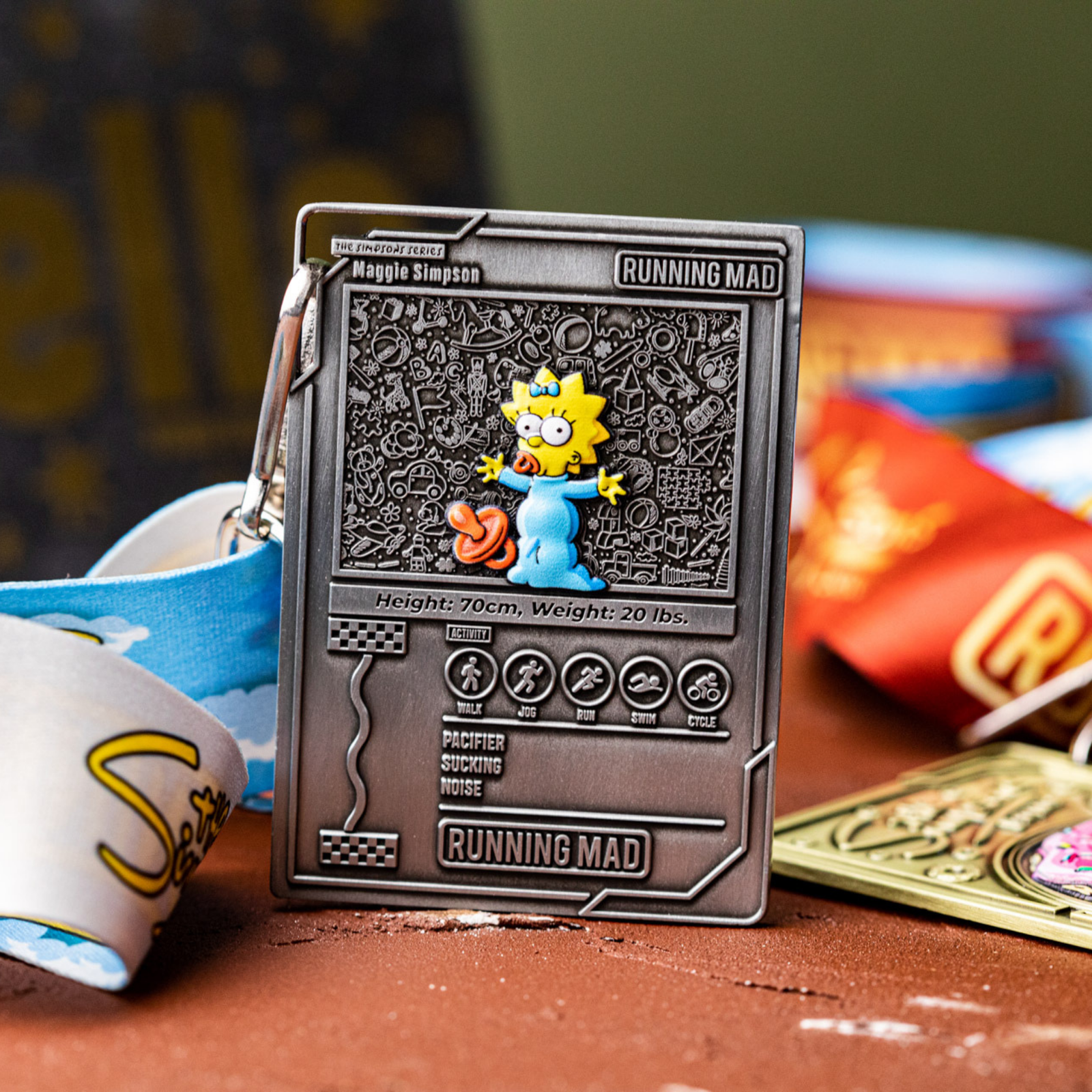 A metal keychain featuring a raised image of an animated character with a pacifier. The background has detailed designs and measurements like height and weight. A colorful lanyard is attached, resting on a wooden surface.