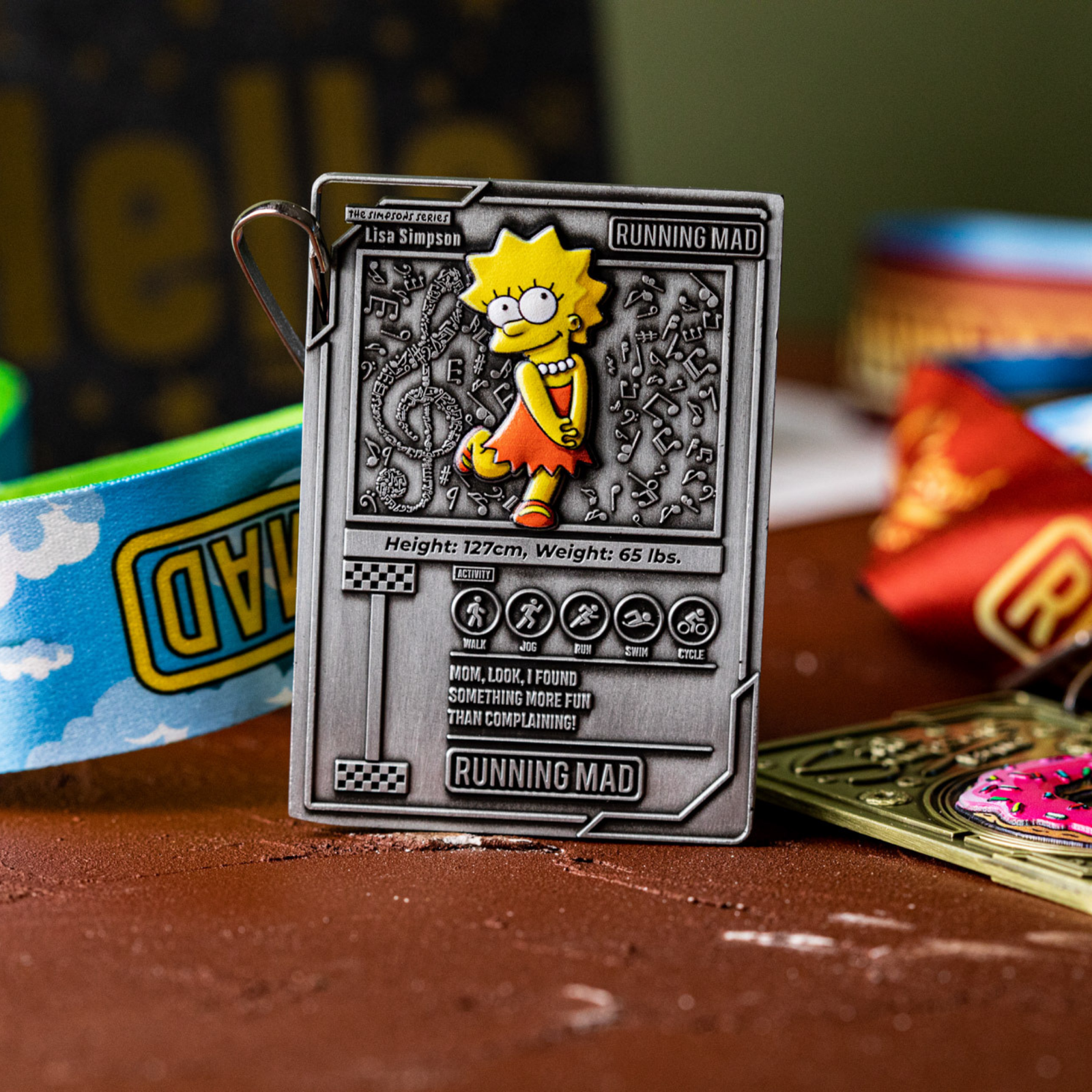 A medal featuring an animated character with spiky hair and an orange dress, set in a card-like design. The medal includes text details like height and weight. Colorful ribbons lie in the background on a brown surface.