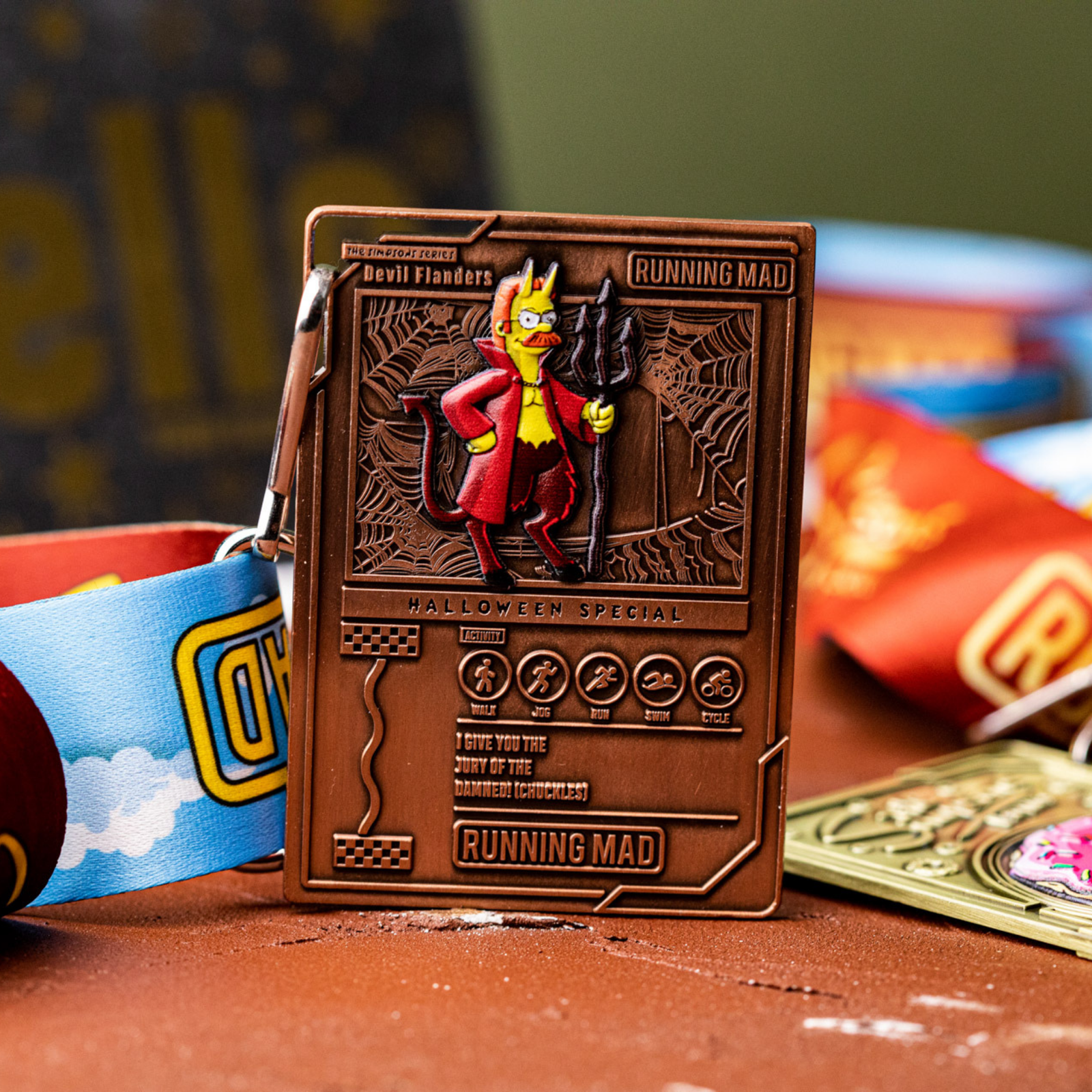 A Halloween-themed medal featuring a cartoon character dressed as a devil, holding a trident. The medal is labeled "Running Mad" and "Devil Flanders Halloween Special." It hangs on a colorful ribbon.