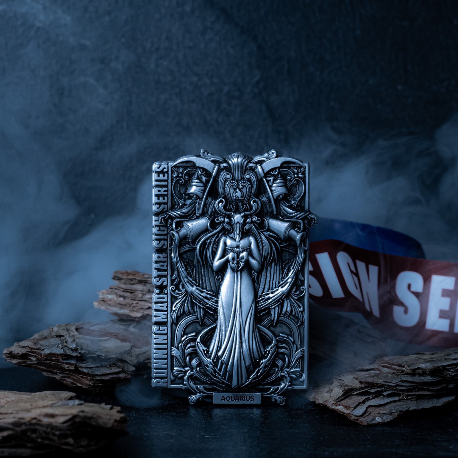 A detailed metallic sculpture with intricate designs, labeled "Aquarius," rests on a smoky surface surrounded by wood pieces. It stands before a backdrop of mist, creating a mysterious and atmospheric setting.