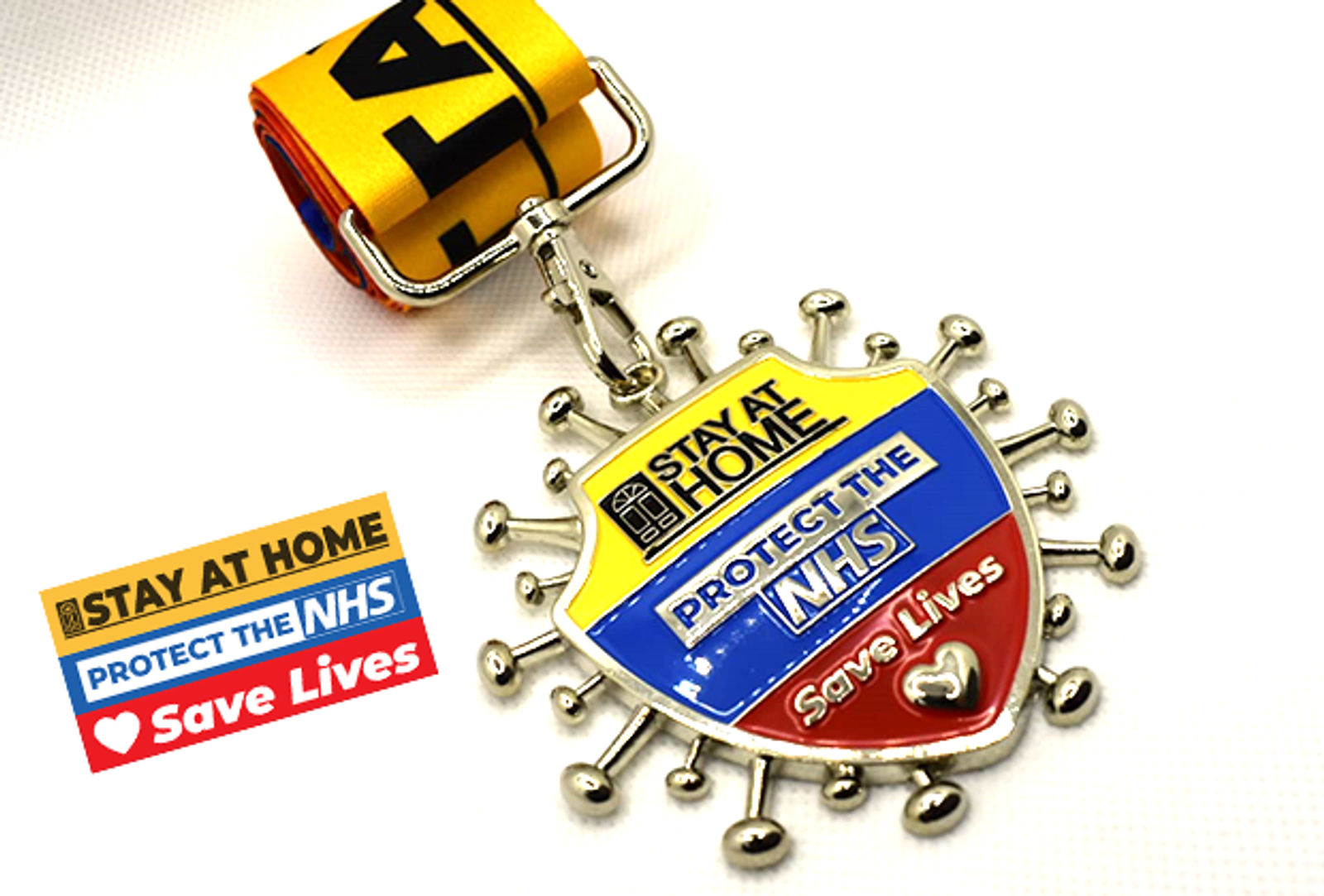 A medal with a striped yellow, blue, and red ribbon, featuring the slogans "Stay at Home," "Protect the NHS," and "Save Lives." The medal design resembles a virus shape with a heart symbol at the bottom and a sturdy clasp.