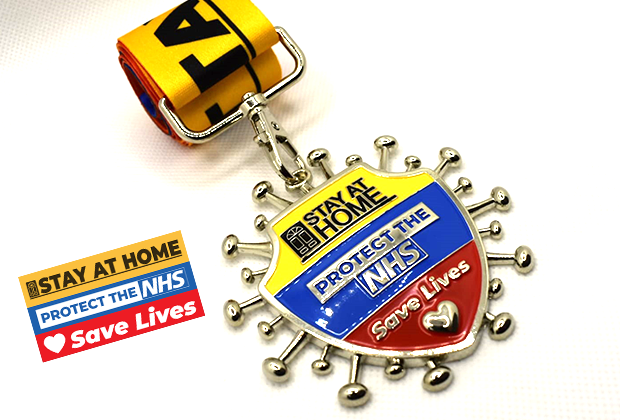 A medal with a striped yellow, blue, and red ribbon, featuring the slogans "Stay at Home," "Protect the NHS," and "Save Lives." The medal design resembles a virus shape with a heart symbol at the bottom and a sturdy clasp.