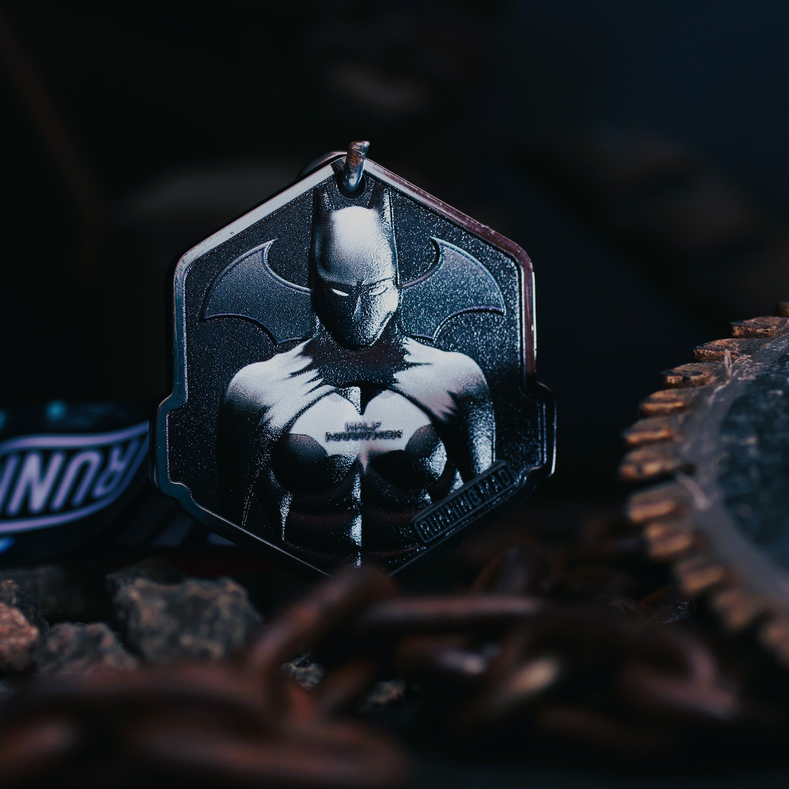 A dark-toned pendant featuring a stylized superhero figure with bat-like ear and wing motifs. It's surrounded by chains and gritty textures, evoking a moody, atmospheric feel.