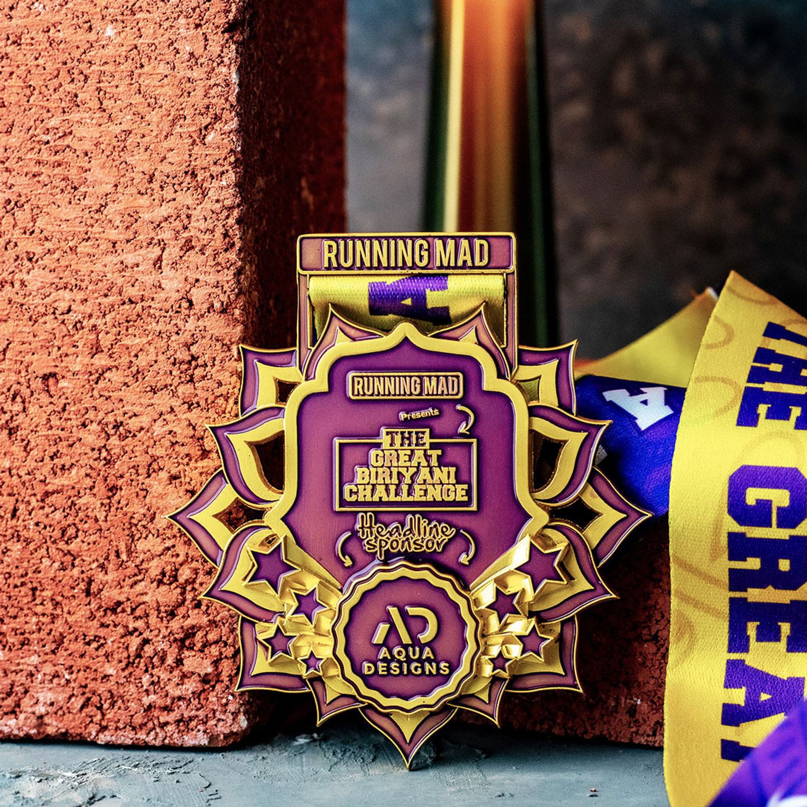 A gold and purple medal with the text "The Great Biryani Challenge" and a "Running Mad" ribbon is displayed against a brick backdrop. A yellow ribbon with part of the word "Great" is visible on the side.