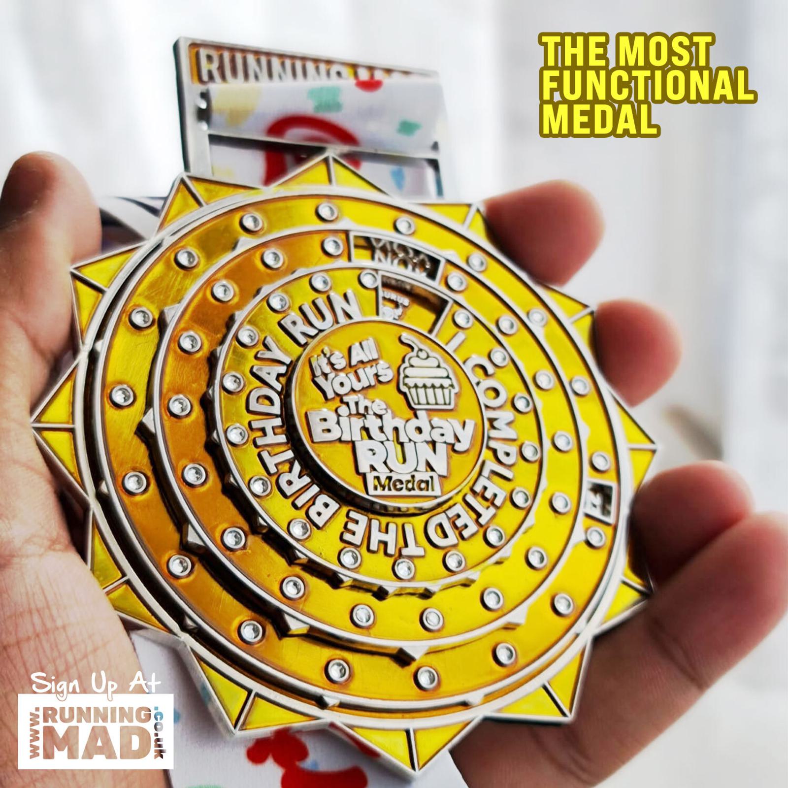 A hand holds a bright yellow circular medal with multiple layers featuring the text "It's Your Birthday Run." The medal has an intricate design resembling gears. Text in the image reads, "The Most Functional Medal" and "Sign Up At RunningMad.co.uk.