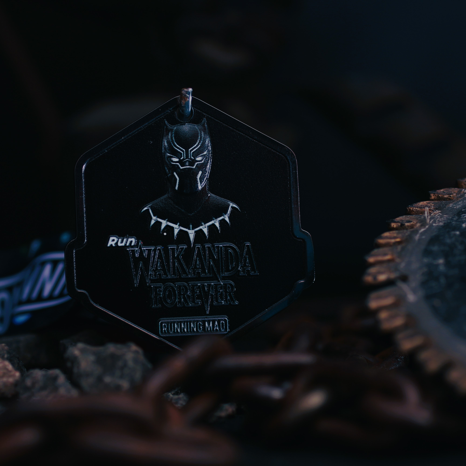 A dark-themed medal featuring a design inspired by Black Panther with the text "Wakanda Forever" and "Running Mad" on it. The medal is hexagonal, with a Panther symbol at the top, set against a dimly lit background.