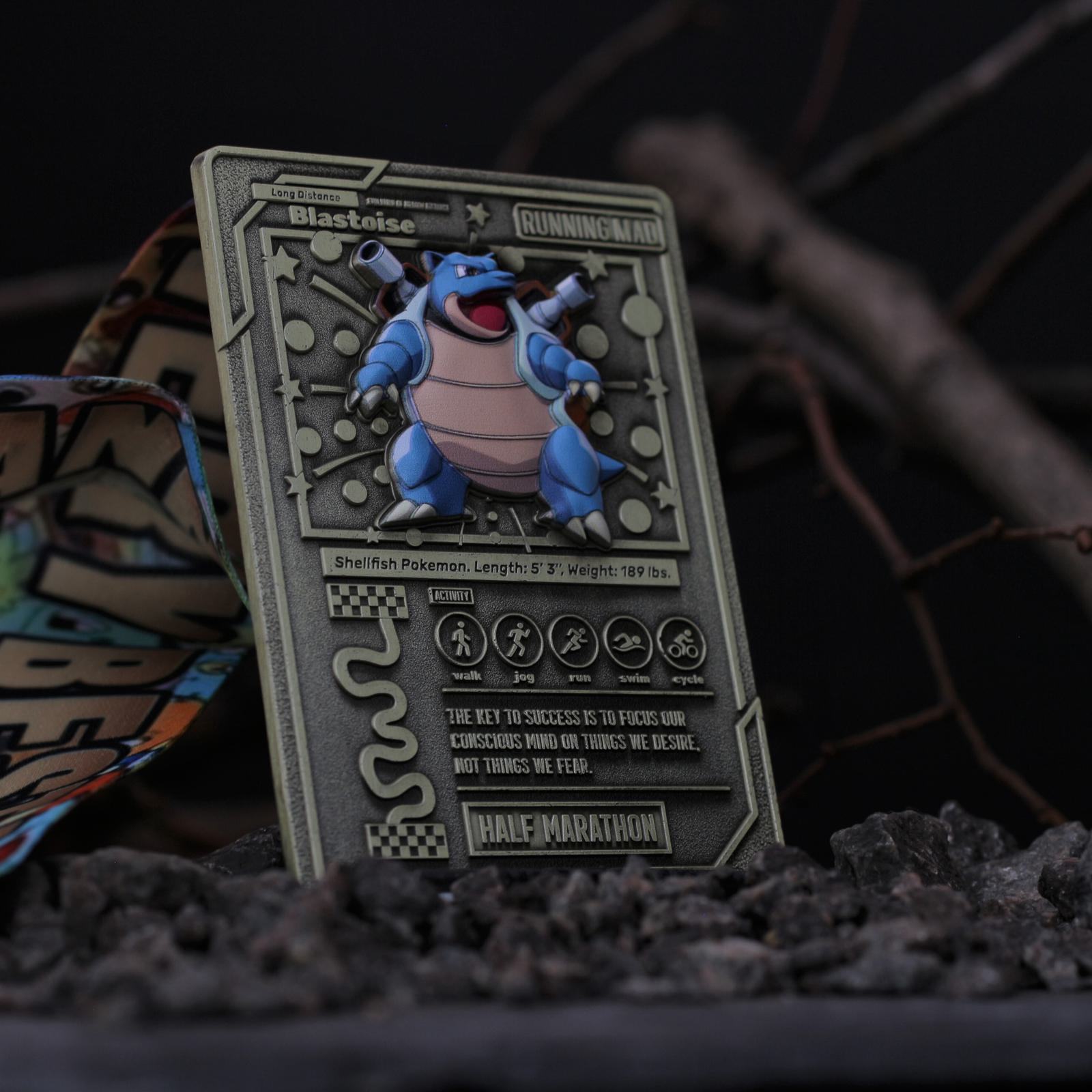 A Blastoise-themed metal card lies on a dark, rocky surface with branches in the background. The card features an intricate design, including race-themed labels like "Runningman" and "Half Marathon," and details about the Blastoise character.