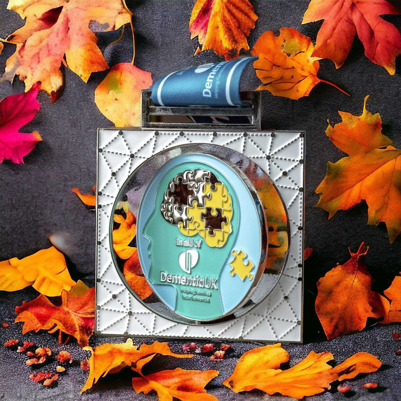 A decorated container with a jigsaw puzzle skull design labeled "Dementia UK" sits amidst scattered autumn leaves. The container features a diamond pattern and an open lid with a leaflet inside.