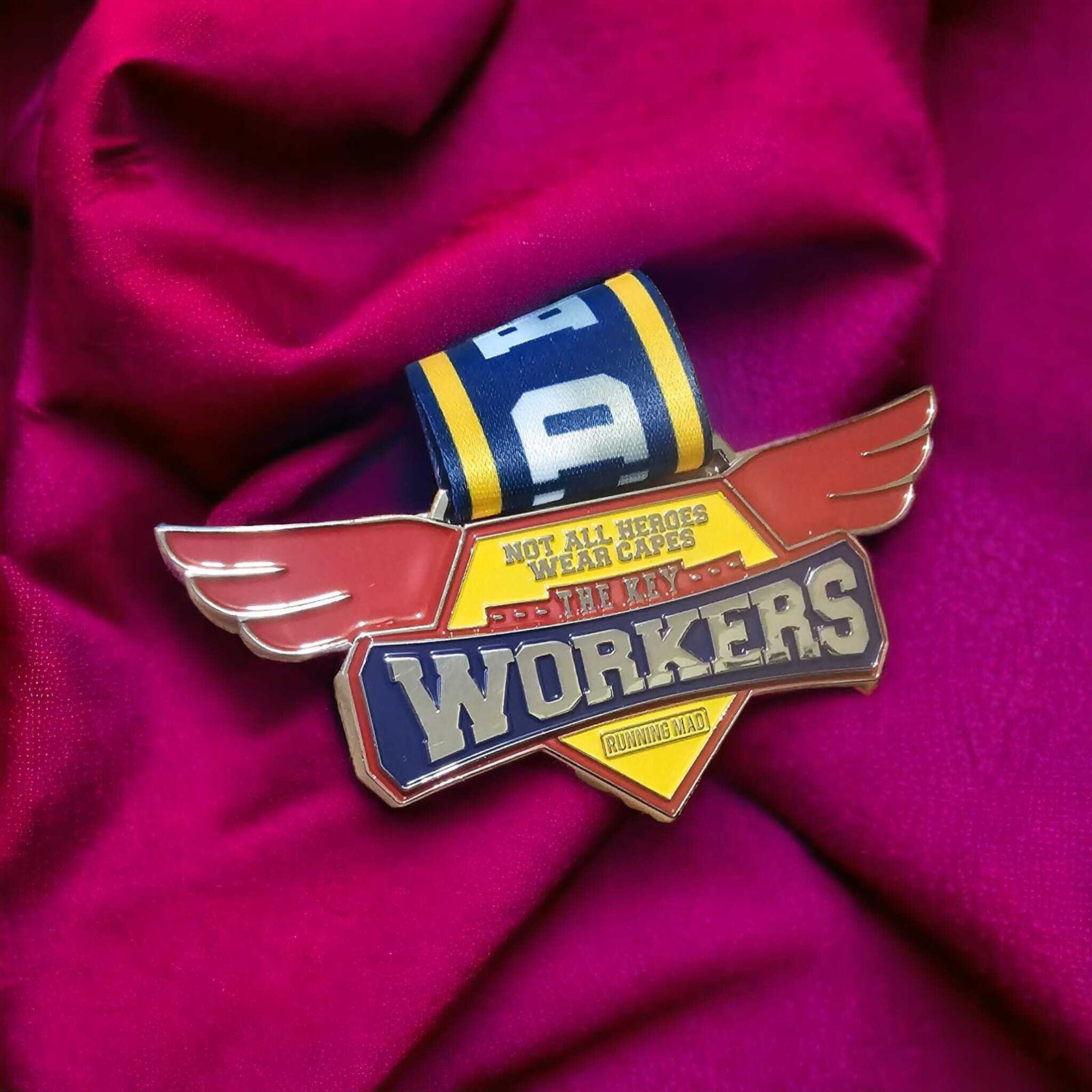 A colorful badge on a red fabric background features wings and the text "Not all heroes wear capes, they are workers." A blue and yellow ribbon with the number 9 is attached above it.