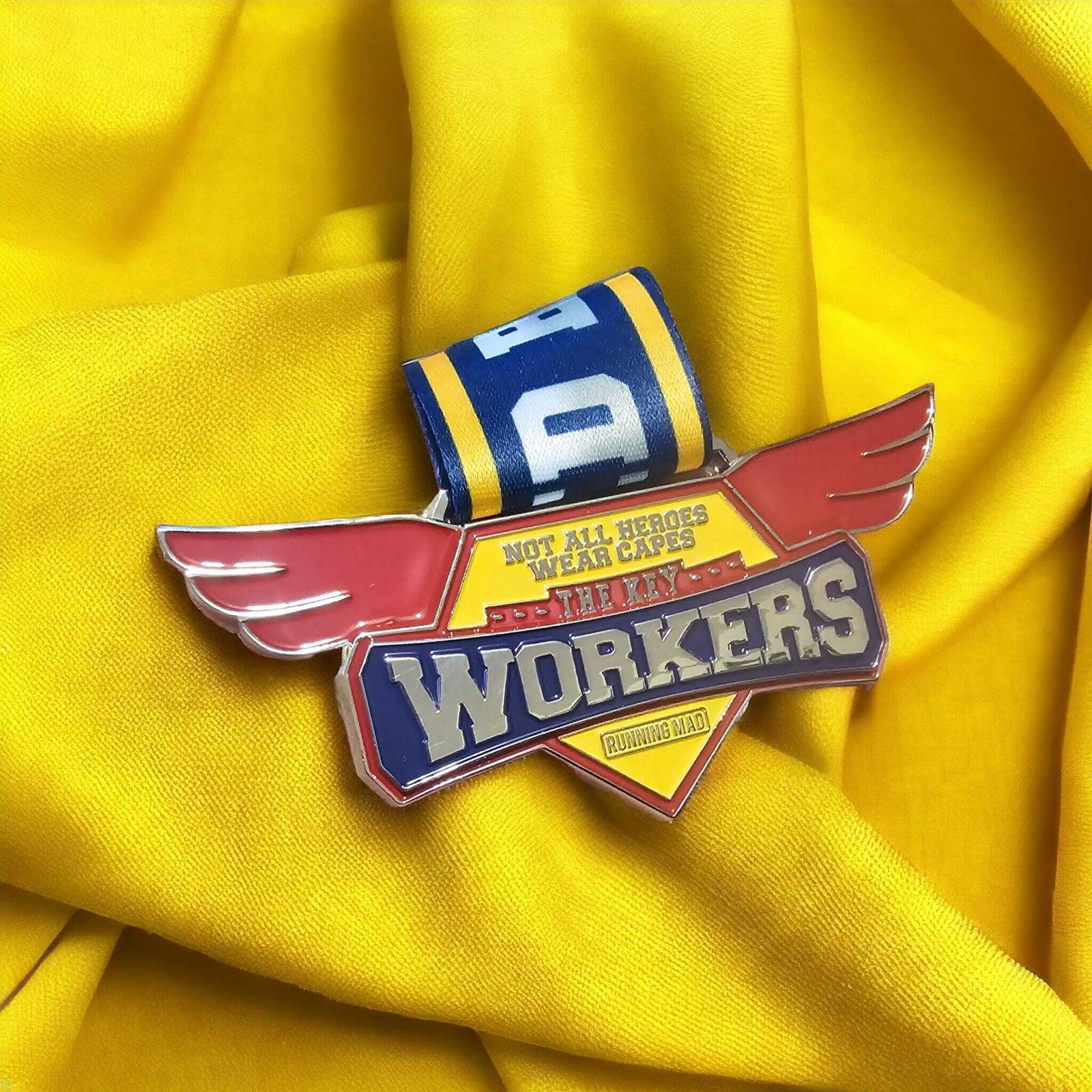 A colorful pin with wings and a scroll that reads "Not all heroes wear capes, they are workers" is placed on a yellow fabric background.