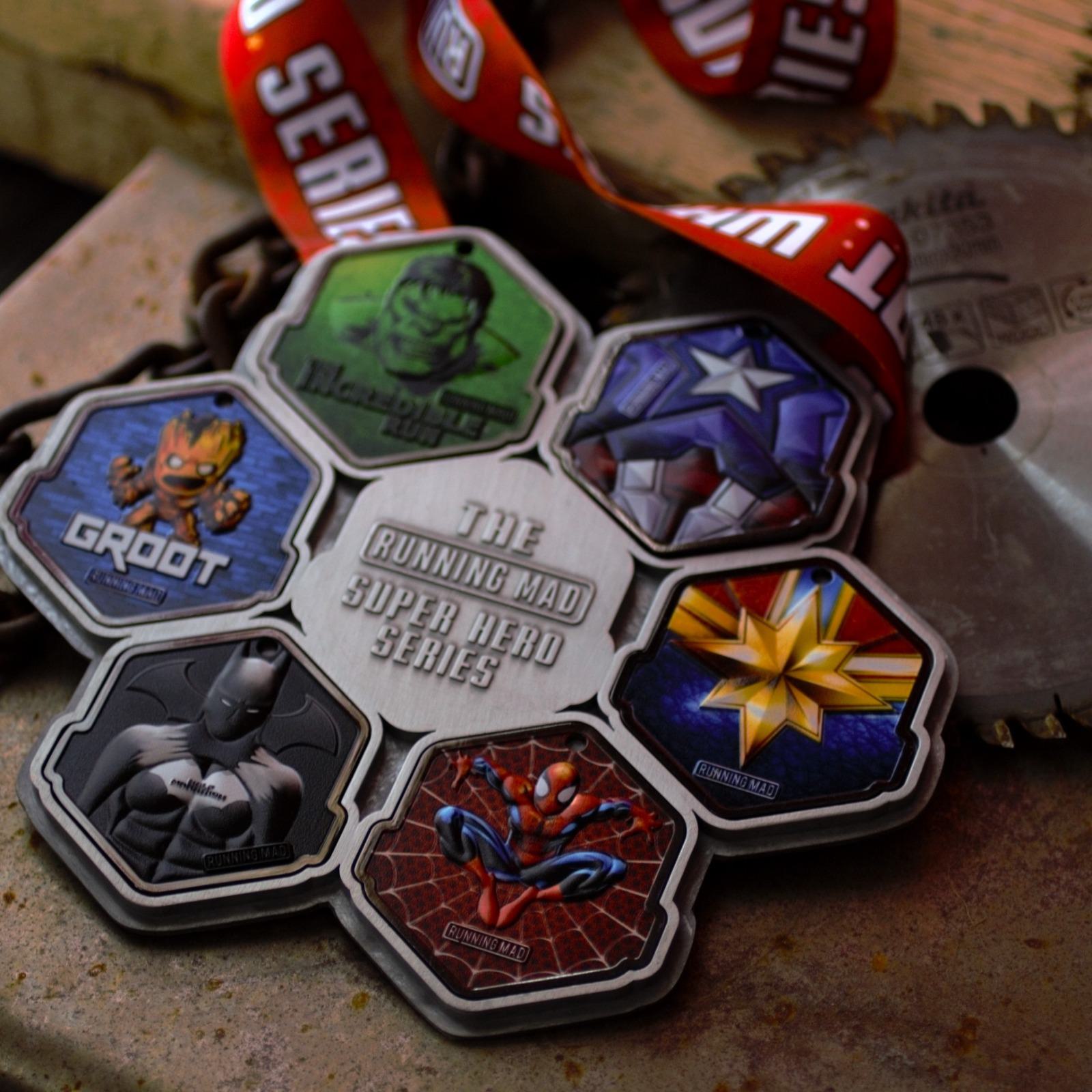 A medal from "The Running Mad Super Hero Series" featuring cartoon-like images of superhero icons Groot, Hulk, Captain America, Captain Marvel, Black Panther, and Spider-Man. The medal is attached to a red lanyard with "SERIES" printed on it.