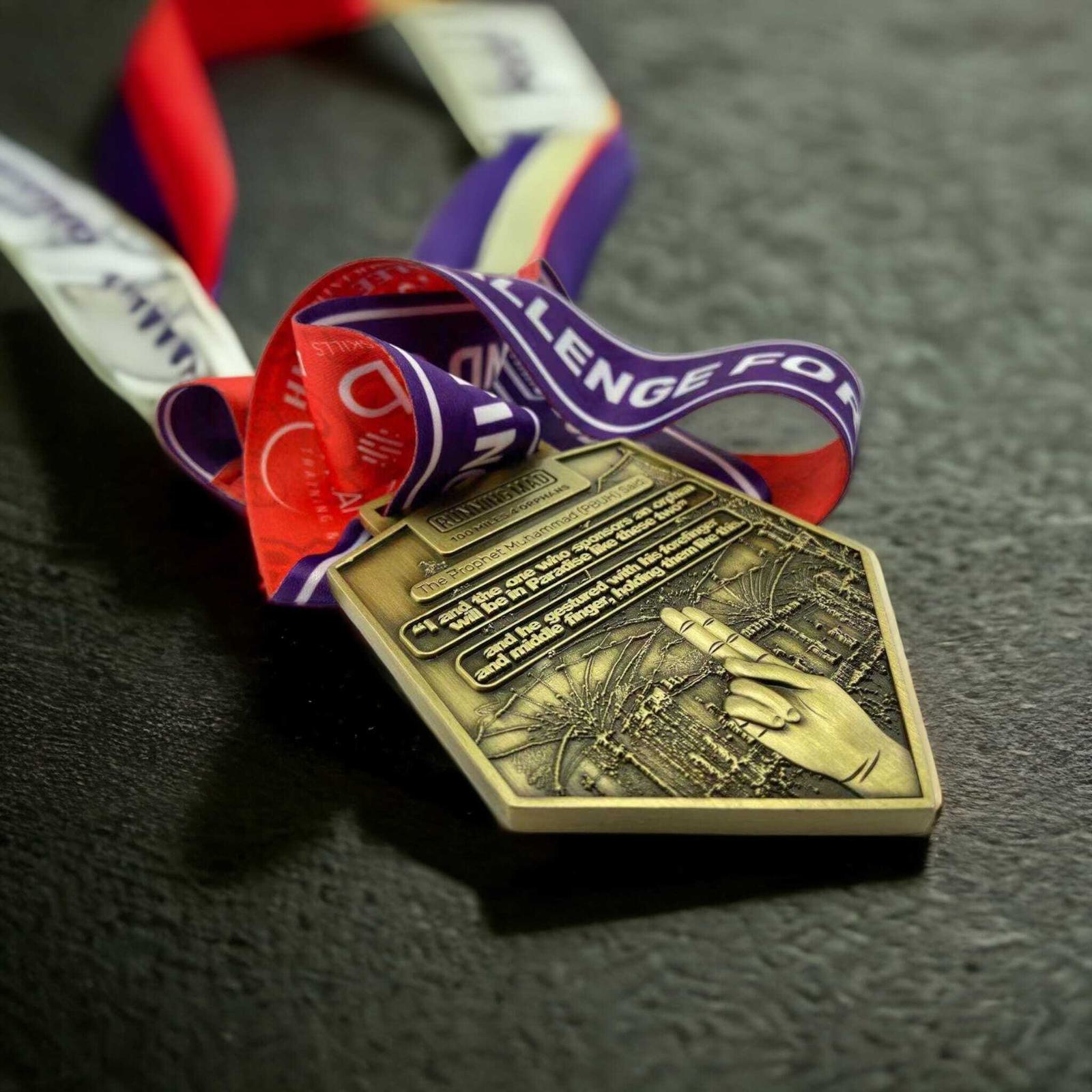 A triangular medal with intricate designs lies on a dark surface. It has red, white, and blue ribbons with text. A hand points to a rocket on the medal, symbolizing a space-themed event.
