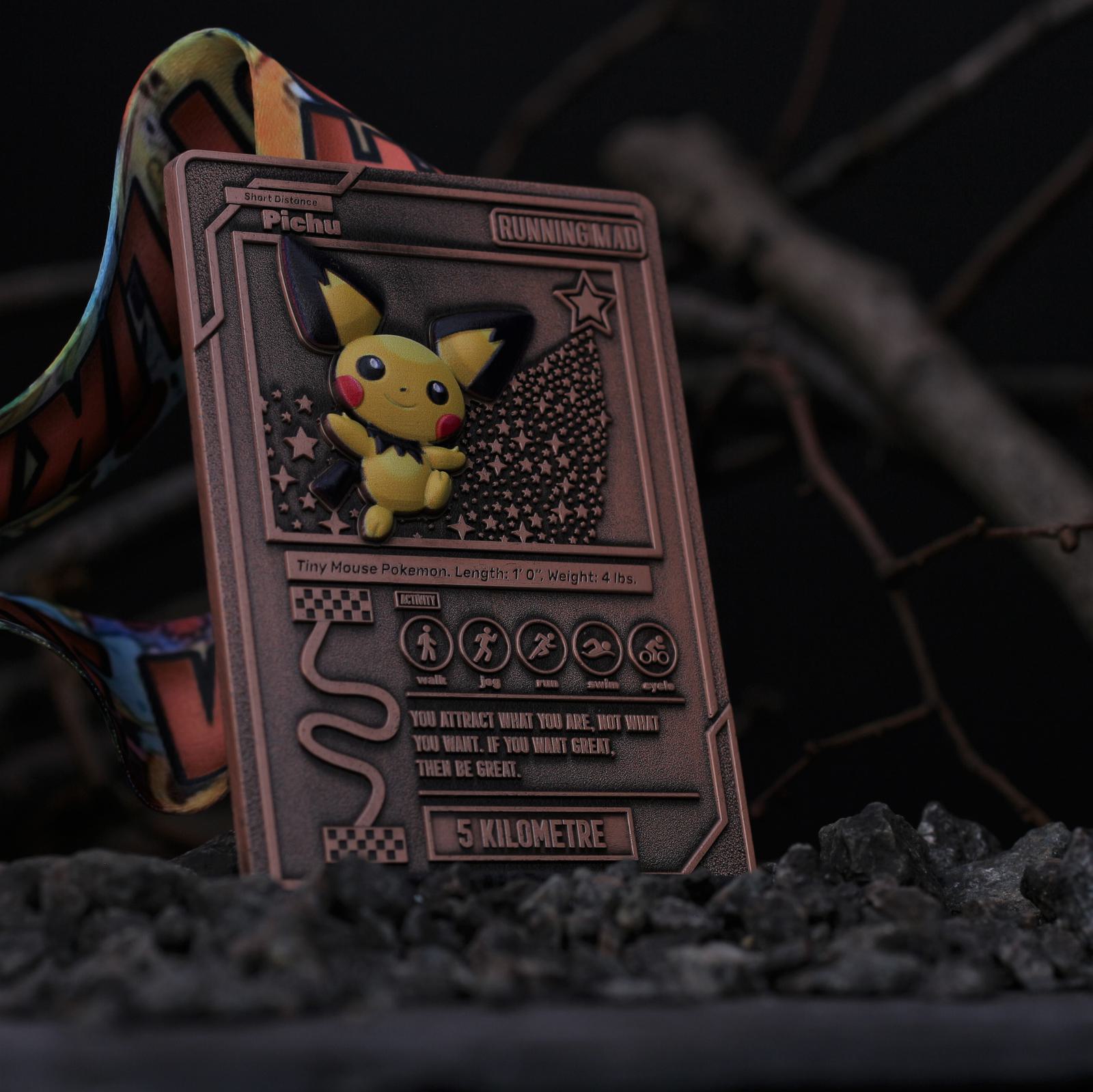 A bronze medal featuring Pichu from Pokémon, displayed among rocks. The medal has various stats and a "5 Kilometre" label, with a colorful ribbon attached.