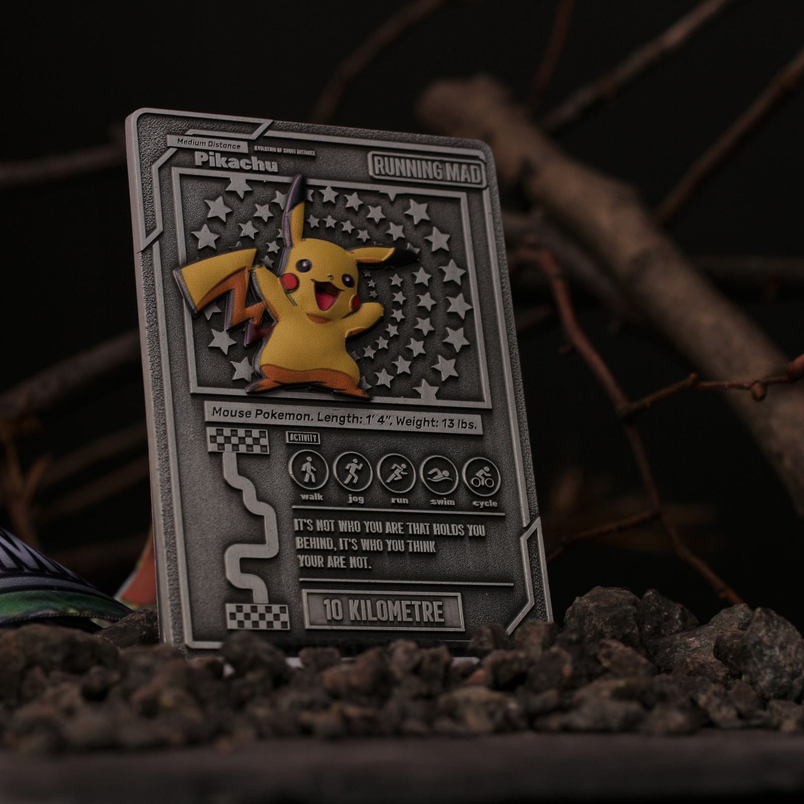 A detailed, metal-look trading card features Pikachu surrounded by a starry design. The card includes stats and is set on a dark, rocky surface with some twigs and leaves around, adding an adventurous, rugged feel.