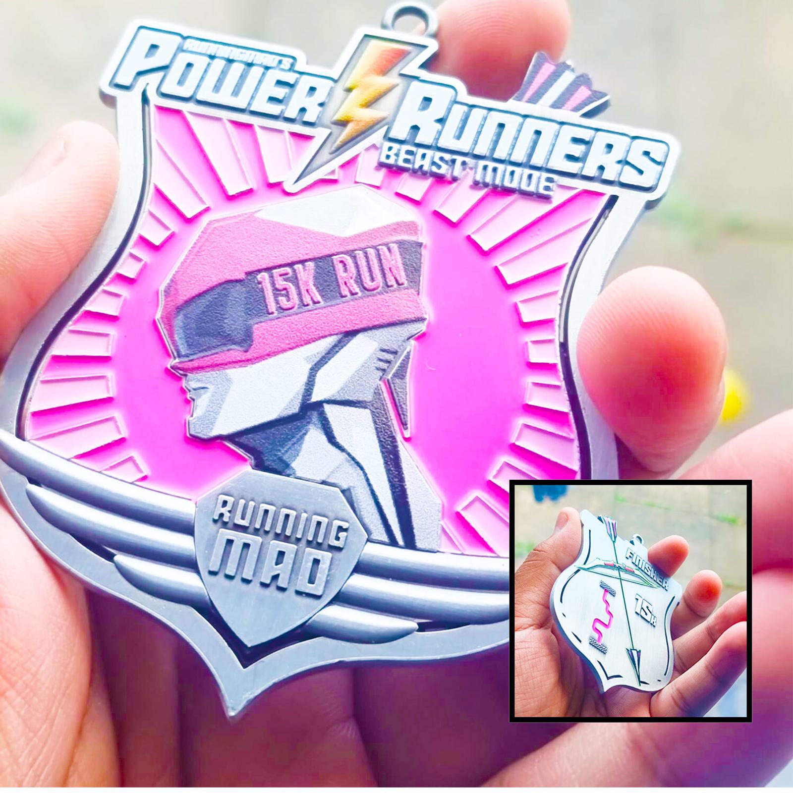Close-up of a hand holding a medal with "Power Runners Beast Mode" and "15K Run" text. The design features a stylized runner with a pink background. An inset shows the medal's back with a logo.