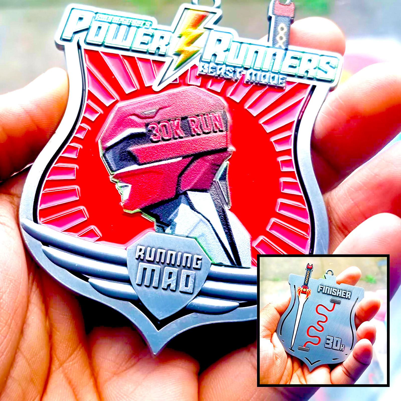 Close-up of a person holding a medal with a Power Rangers theme, featuring an embossed helmet and text "30K Run, Running Mad." An inset shows the back of the medal with a map design and the word "Finisher.