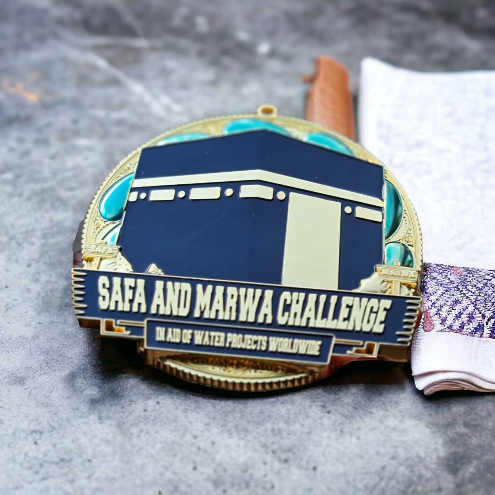 A round medal for the "Safa and Marwa Challenge" lies on a textured surface. The design features an illustration of a mosque. There's a strap attached to the medal, partially visible, resting near a folded cloth.