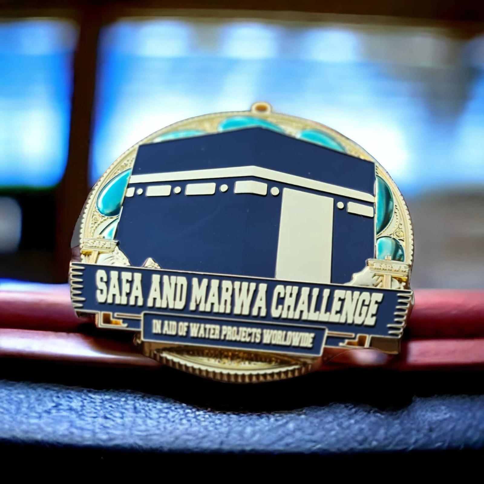 A medal with the text "Safa and Marwa Challenge" and "In aid of water projects worldwide." It features a design resembling the Kaaba, with decorative elements in blue and gold.