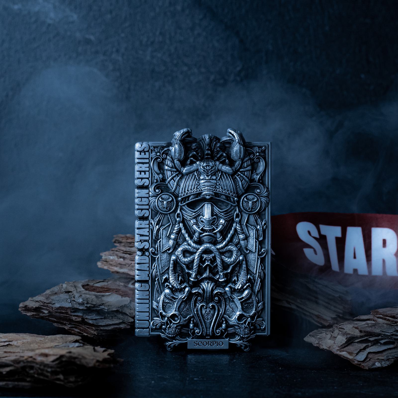 Intricate metallic sculpture of a Scorpio zodiac symbol with detailed engravings, set against a moody, smoky background. Wood pieces and a partially visible red and white ribbon add depth to the composition.