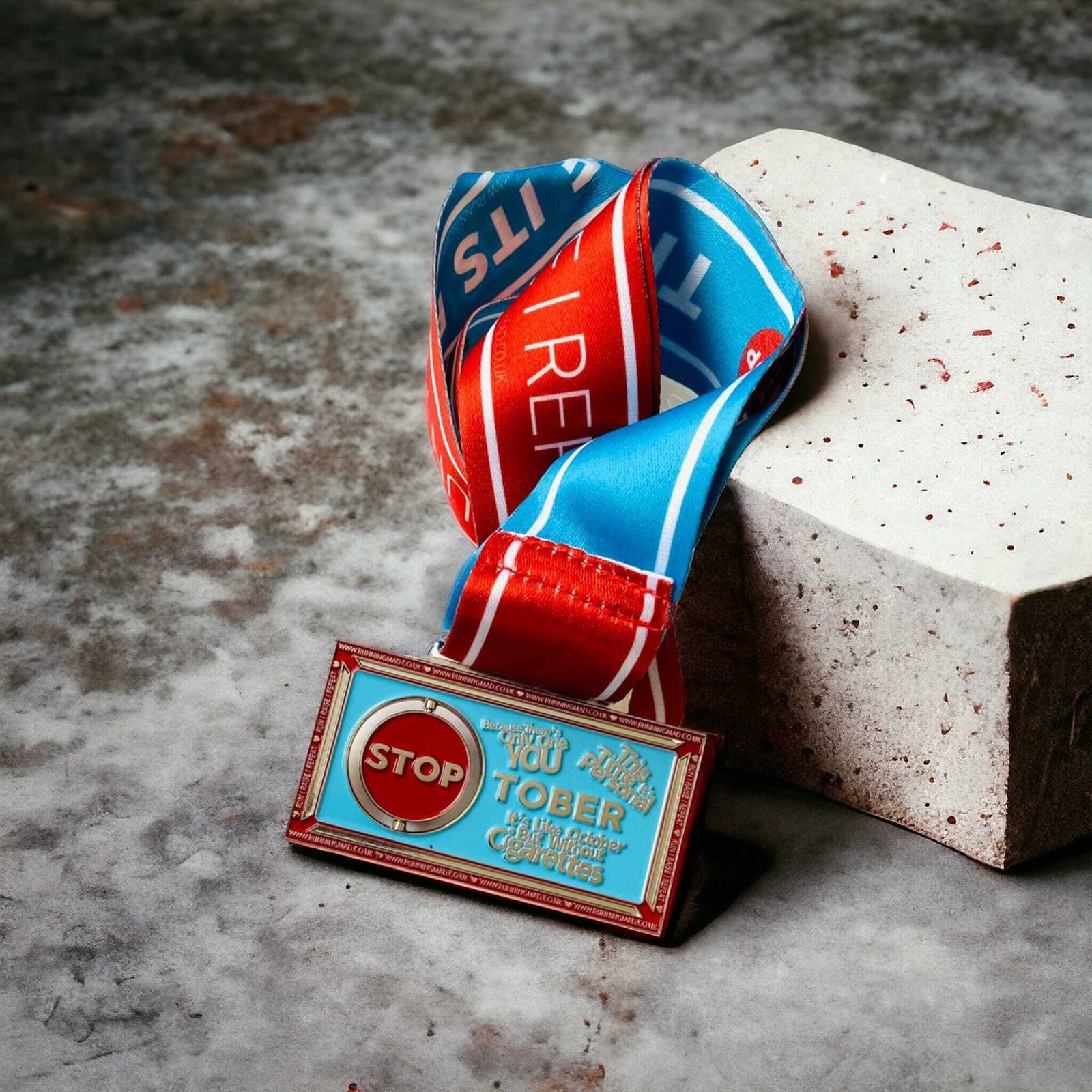 A colorful medal with a "STOP" sign on a blue and red ribbon is resting on a textured, light gray stone. The ribbon is vibrant and features the word "INSPIRE." The medal is propped up for display.