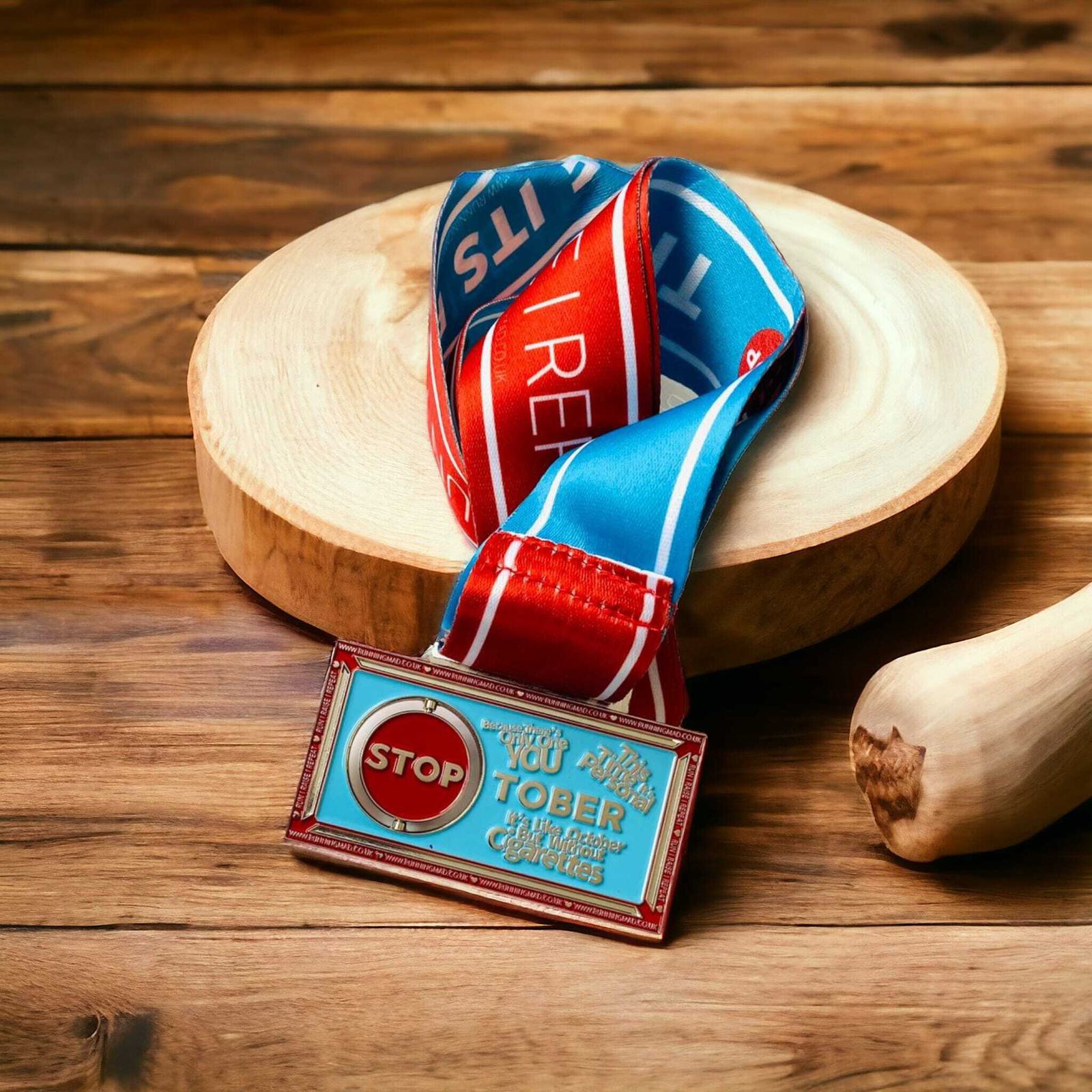 A medal with a red and blue ribbon lies on a round wooden board. The medal features a red stop sign and the text "You Run October Marathon Series." The background is a wooden surface.