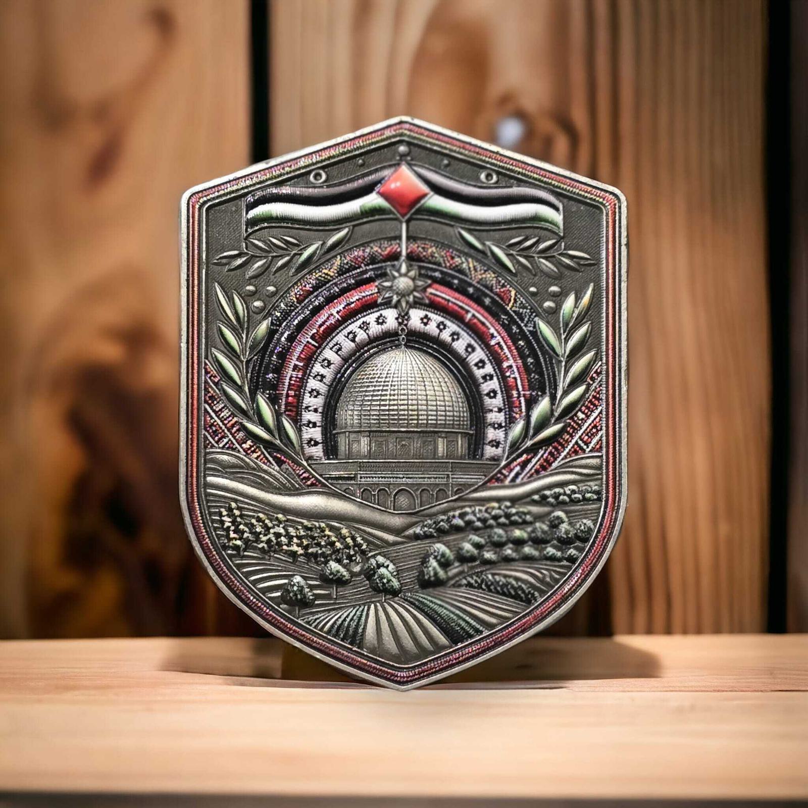 A decorative shield featuring a central dome design with laurel branches and a red diamond shape above. The background depicts rolling hills and fields. The shield rests on a wooden surface.