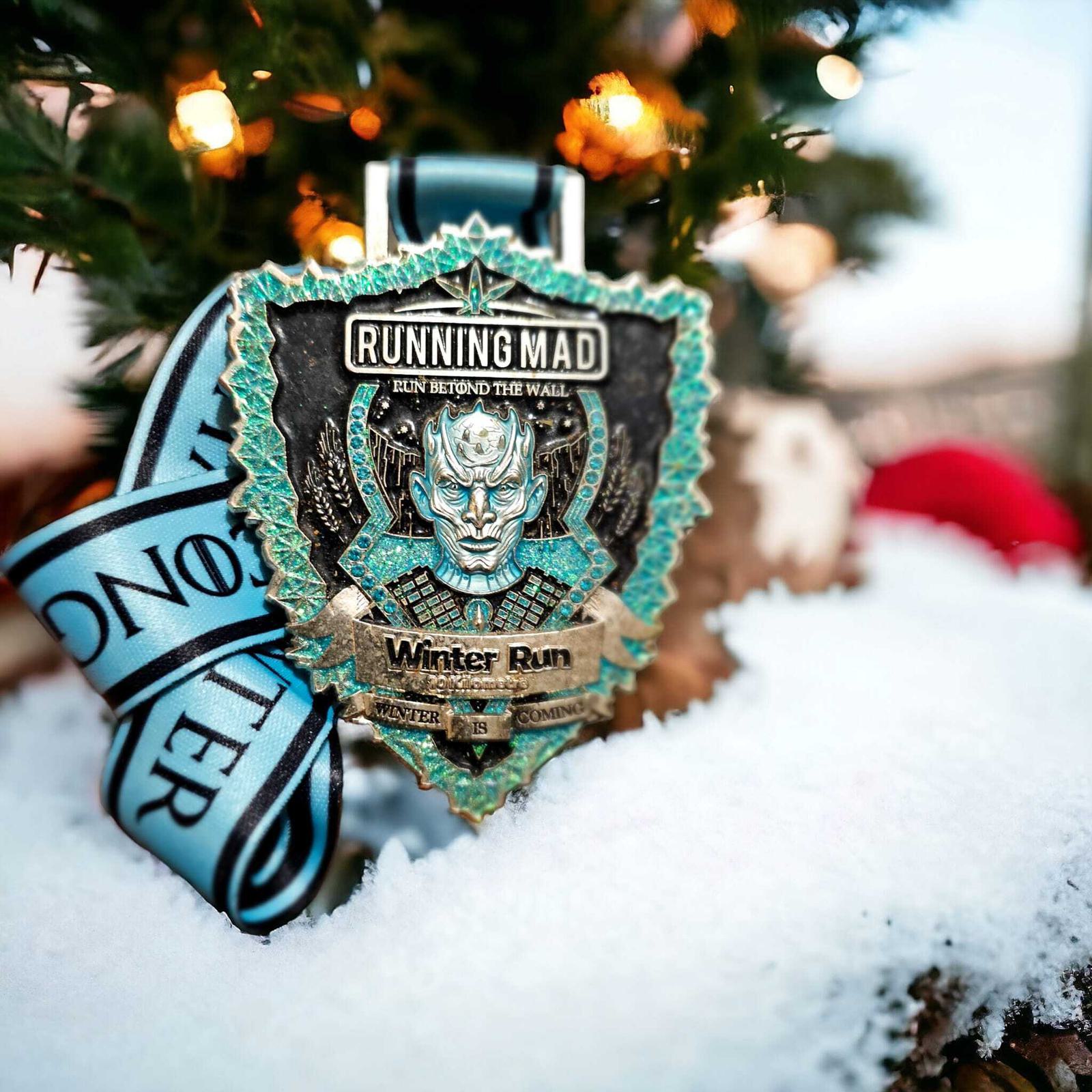 A medal for the "Running Mad Winter Run" hangs on a tree, surrounded by snow. The design features intricate details and a ribbon attached.