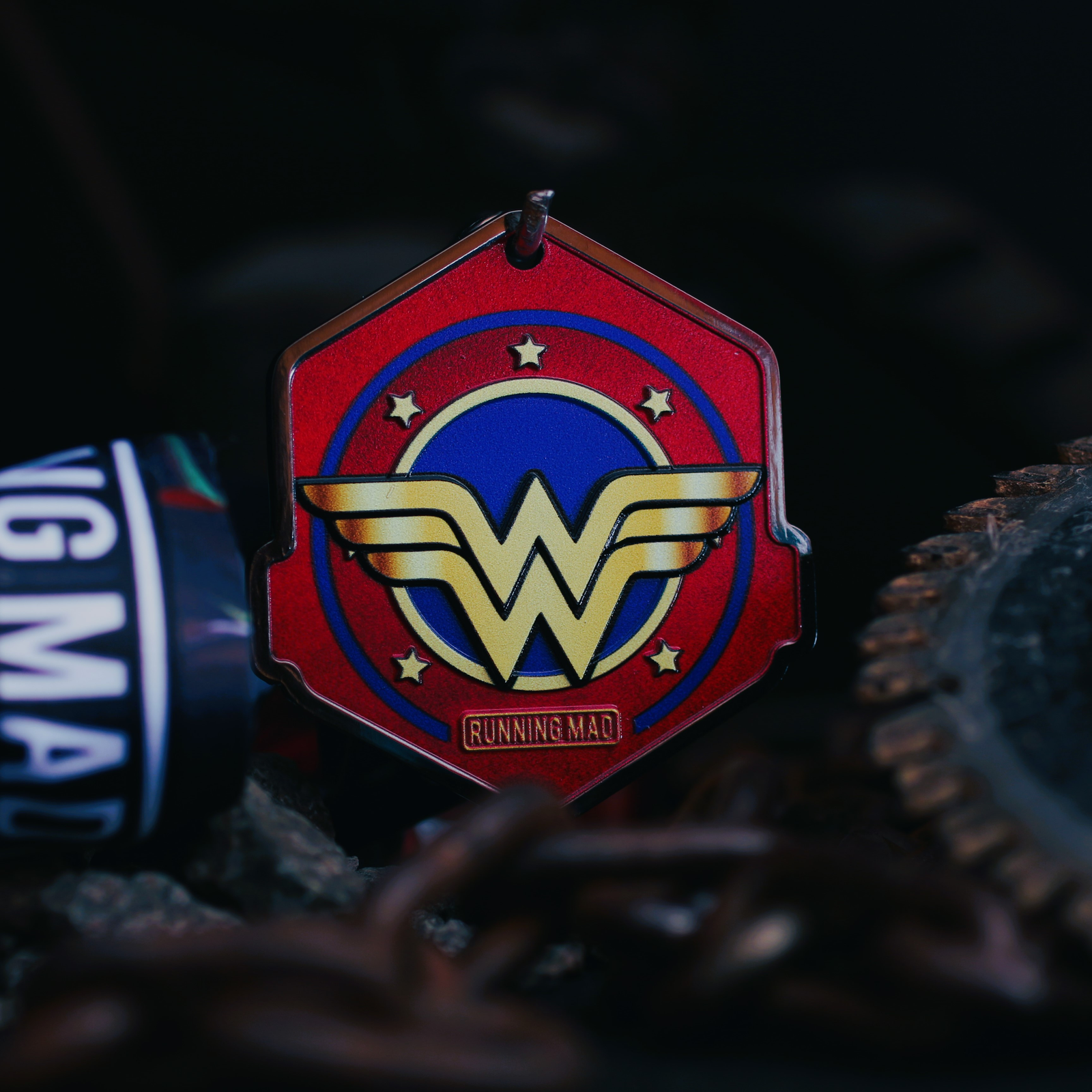 A vibrant medal featuring a stylized "W" in gold over a blue circle, surrounded by stars, set on a red hexagonal background. The medal is accompanied by a bracelet that reads "RUNNING MAD.