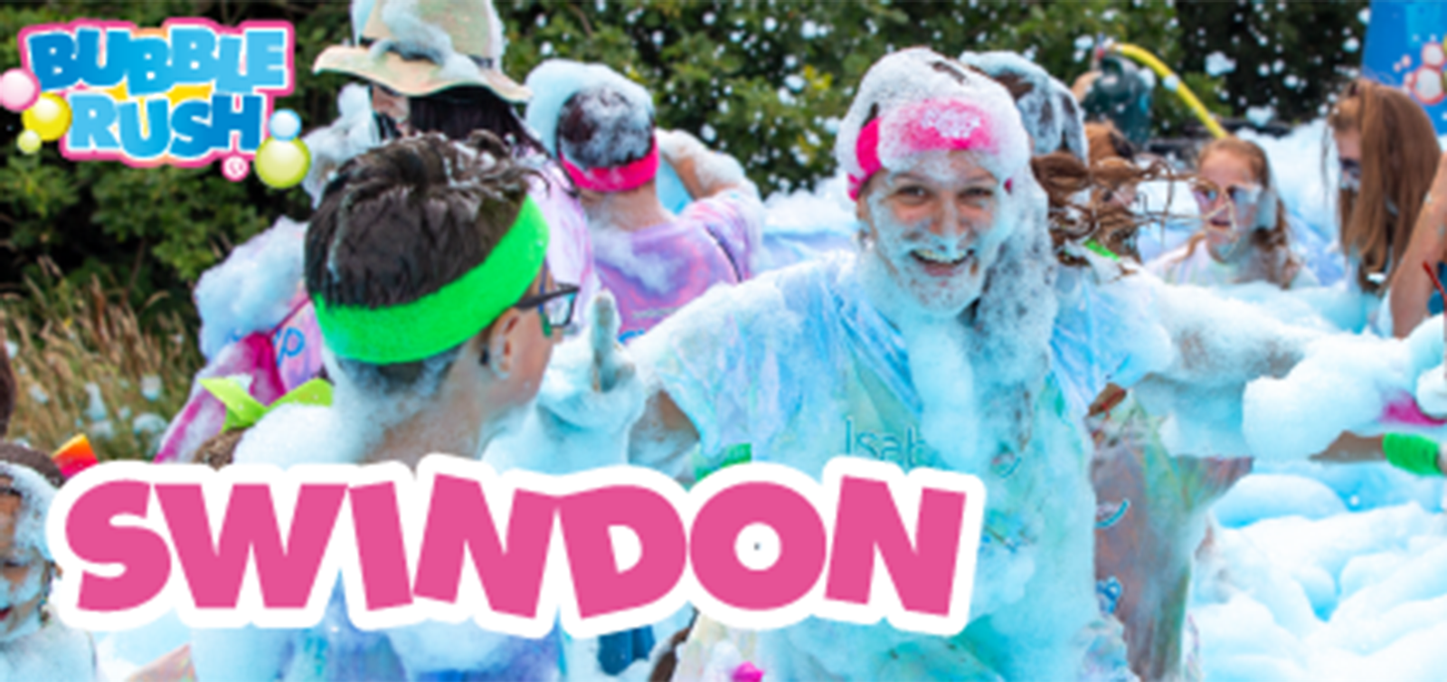 People covered in foam participating in a fun event called "Bubble Rush" in Swindon. They are smiling and enjoying themselves in a bright and bubbly atmosphere.
