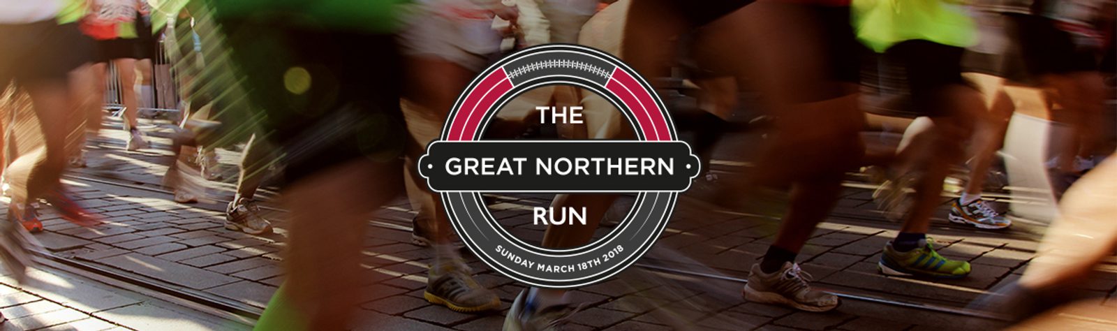 Blurred motion of runners in a street race with the event logo in the center reading "THE GREAT NORTHERN RUN" and the date "SUNDAY MARCH 12TH, 2023." The logo is circular with red, white, and black colors.