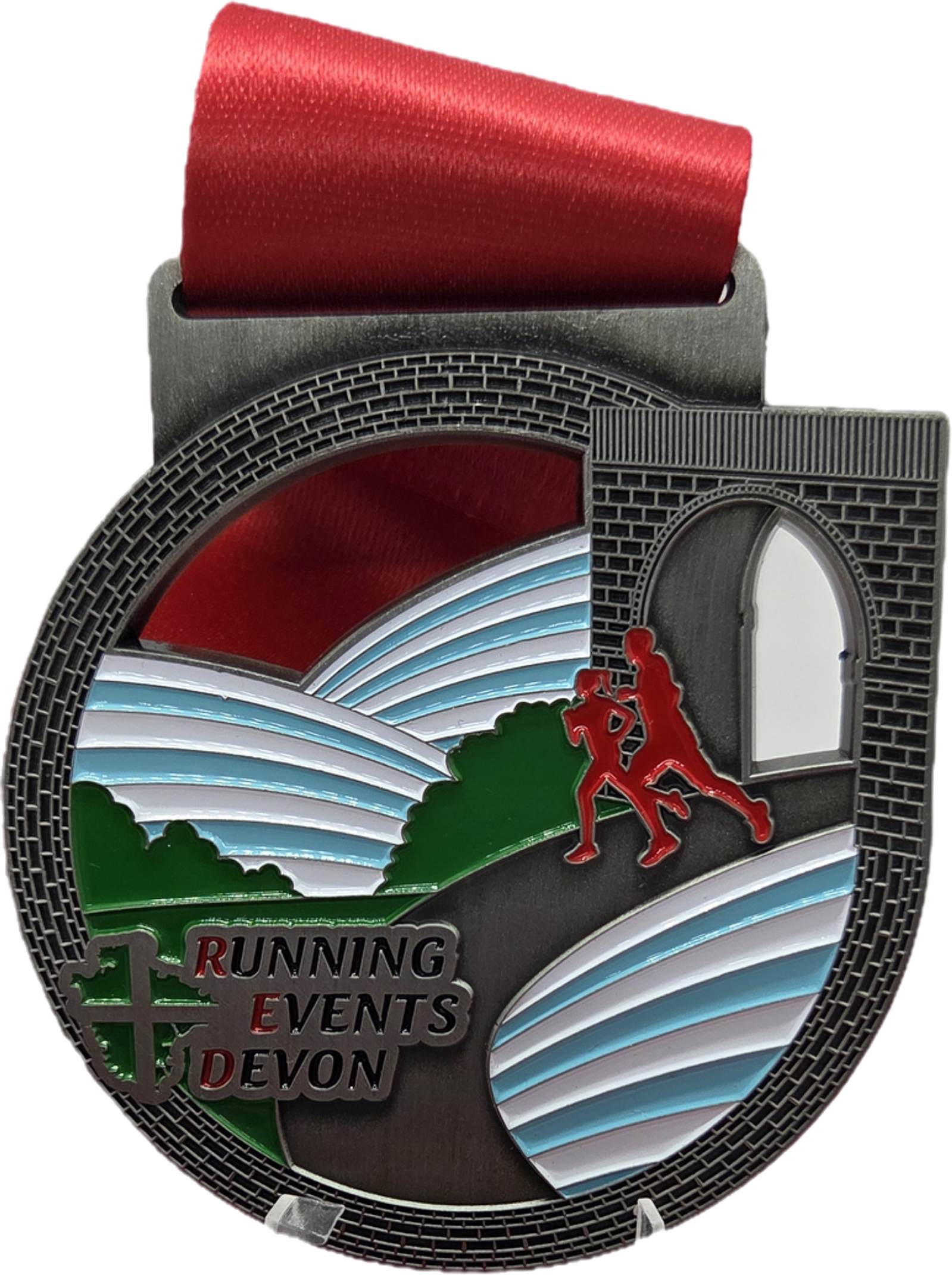 A circular medal with a red ribbon features two red silhouettes of runners, rolling hills, a stone archway, and the text "Running Events Devon" on the lower left in green, white, and red.