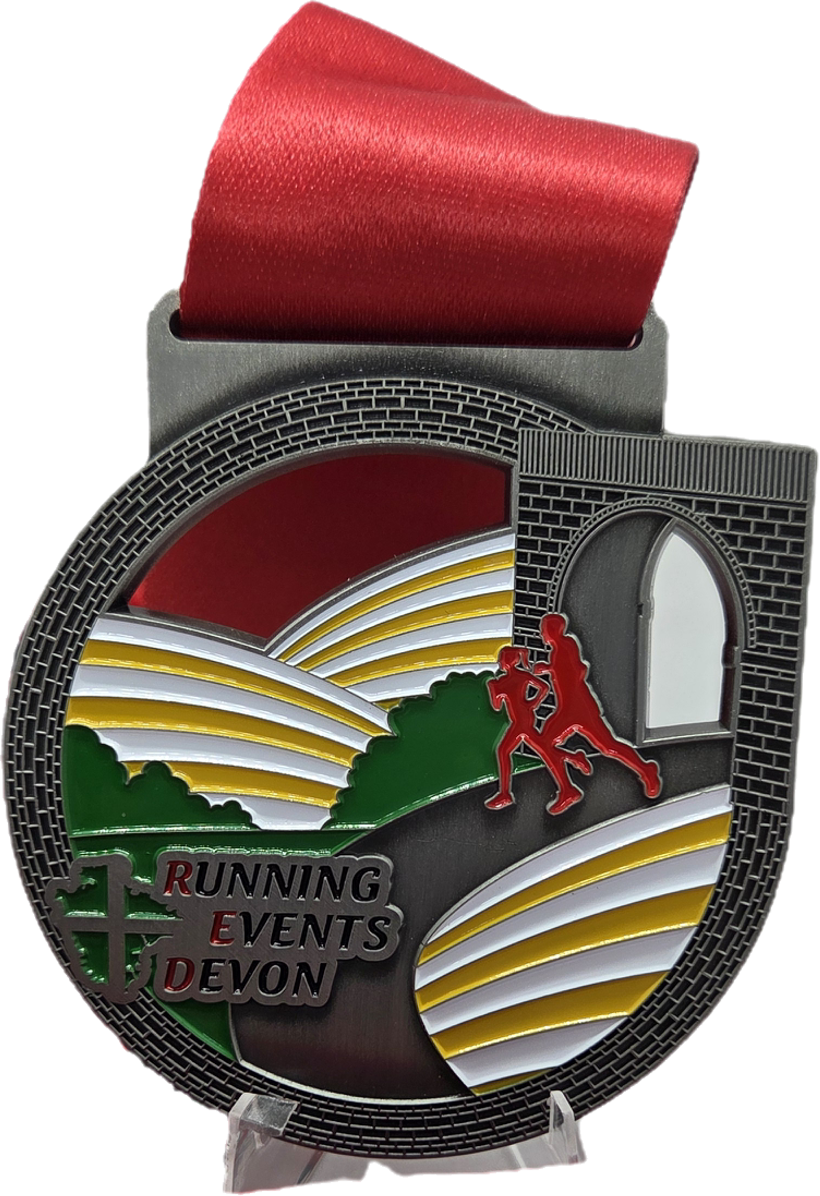 A round medal with a red ribbon features two runners, colorful hills, and an arched bridge. The text “RUNNING EVENTS DEVON” appears at the bottom left in red and green.