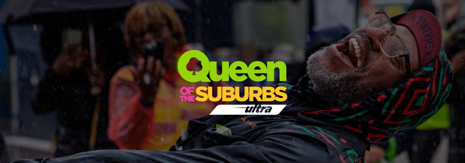 A joyful person in colorful clothing smiles and leans back in the rain. Another person in the background appears to be taking a photo. Overlaid text reads: "Queen of the Suburbs ultra.