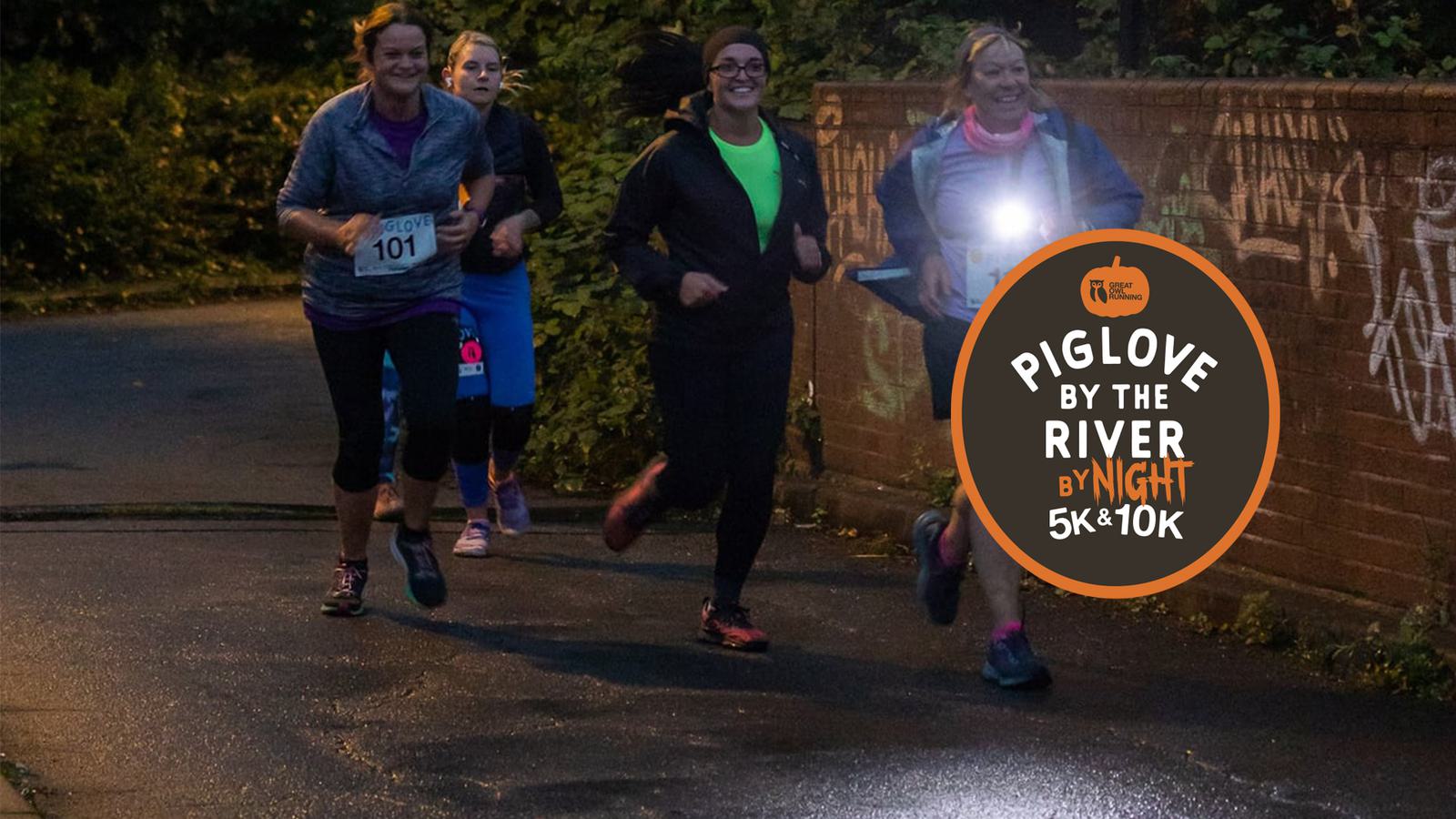 A group of women jogs along a dimly lit path during an evening race. They are wearing athletic gear and are smiling. A round sign on the right reads: "Piglove by the River by Night 5K & 10K.