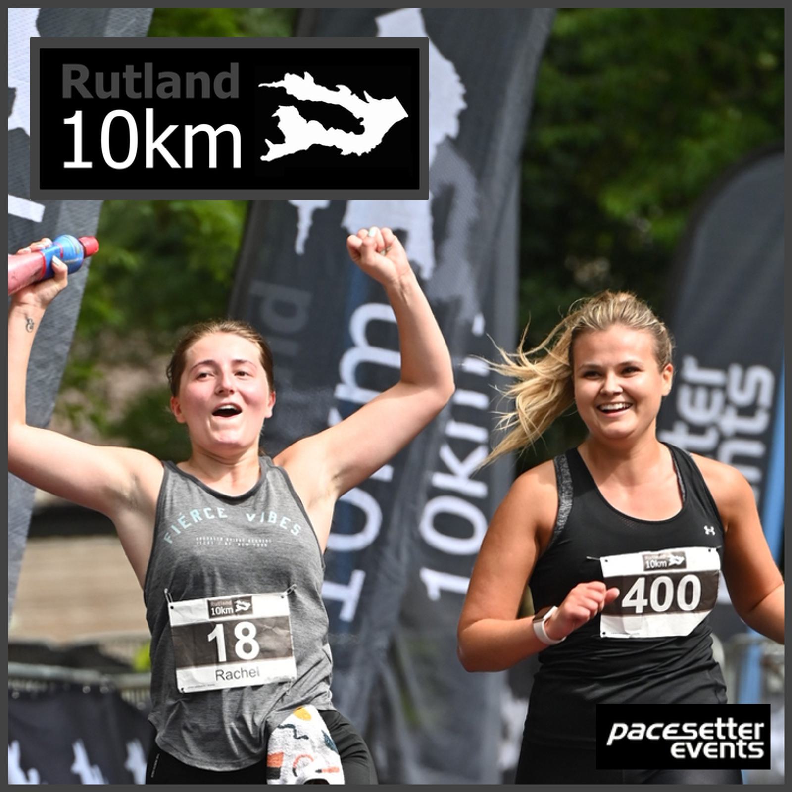 Two women running and smiling in a Rutland 10km race. One has a bib number 18 and the other 400. They hold colorful water bottles, with event flags in the background. The logo "Pacesetter Events" is visible in the corner.