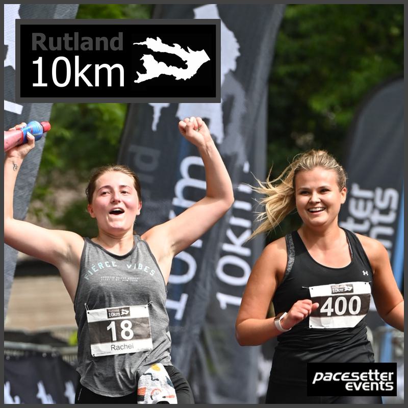 Two women running and smiling in a Rutland 10km race. One has a bib number 18 and the other 400. They hold colorful water bottles, with event flags in the background. The logo "Pacesetter Events" is visible in the corner.