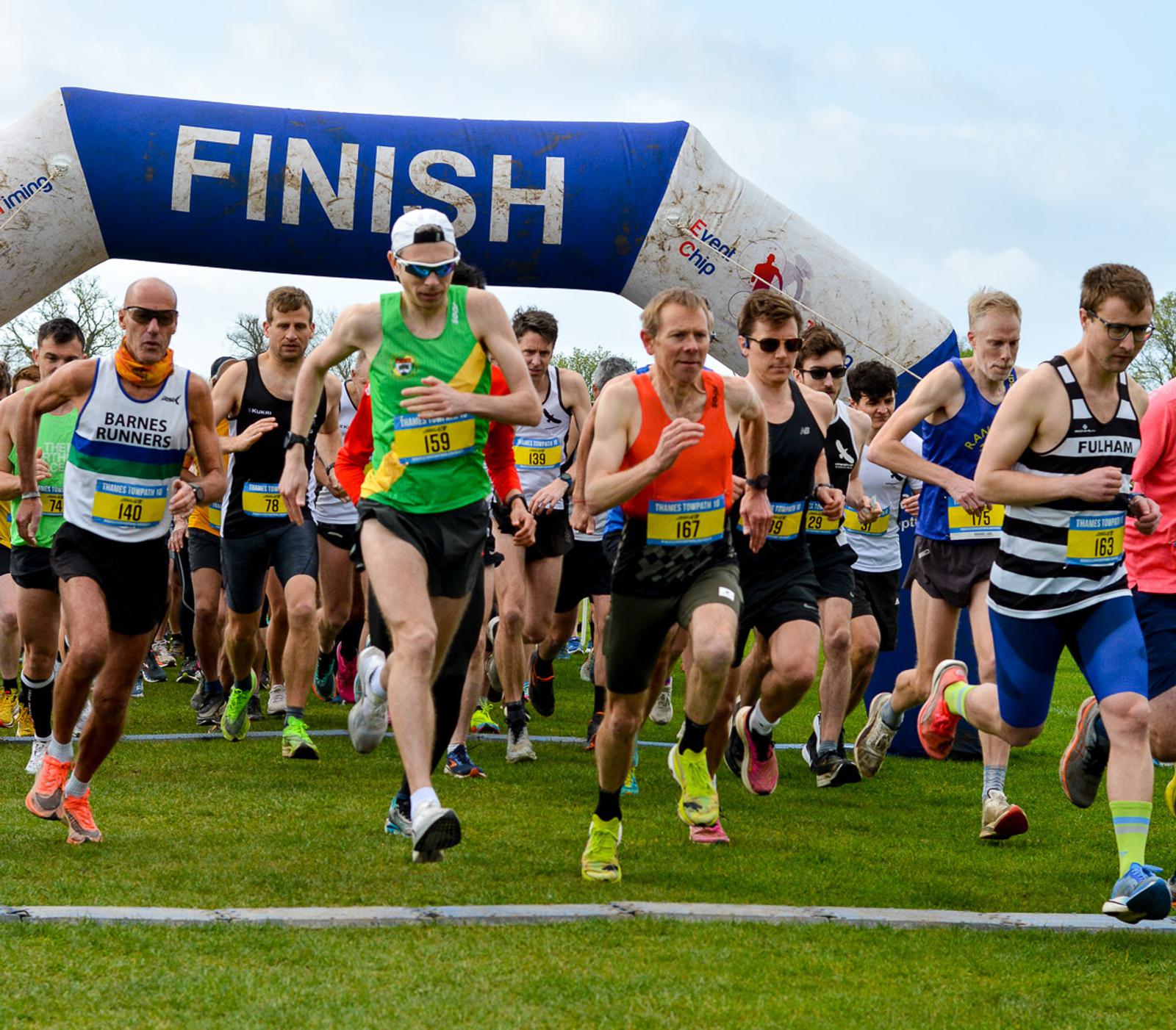 A group of runners starting a race, wearing colorful athletic attire. They are on a grassy field, and an inflatable arch marked "FINISH" is visible in the background. The sky is clear, suggesting a pleasant day for running.